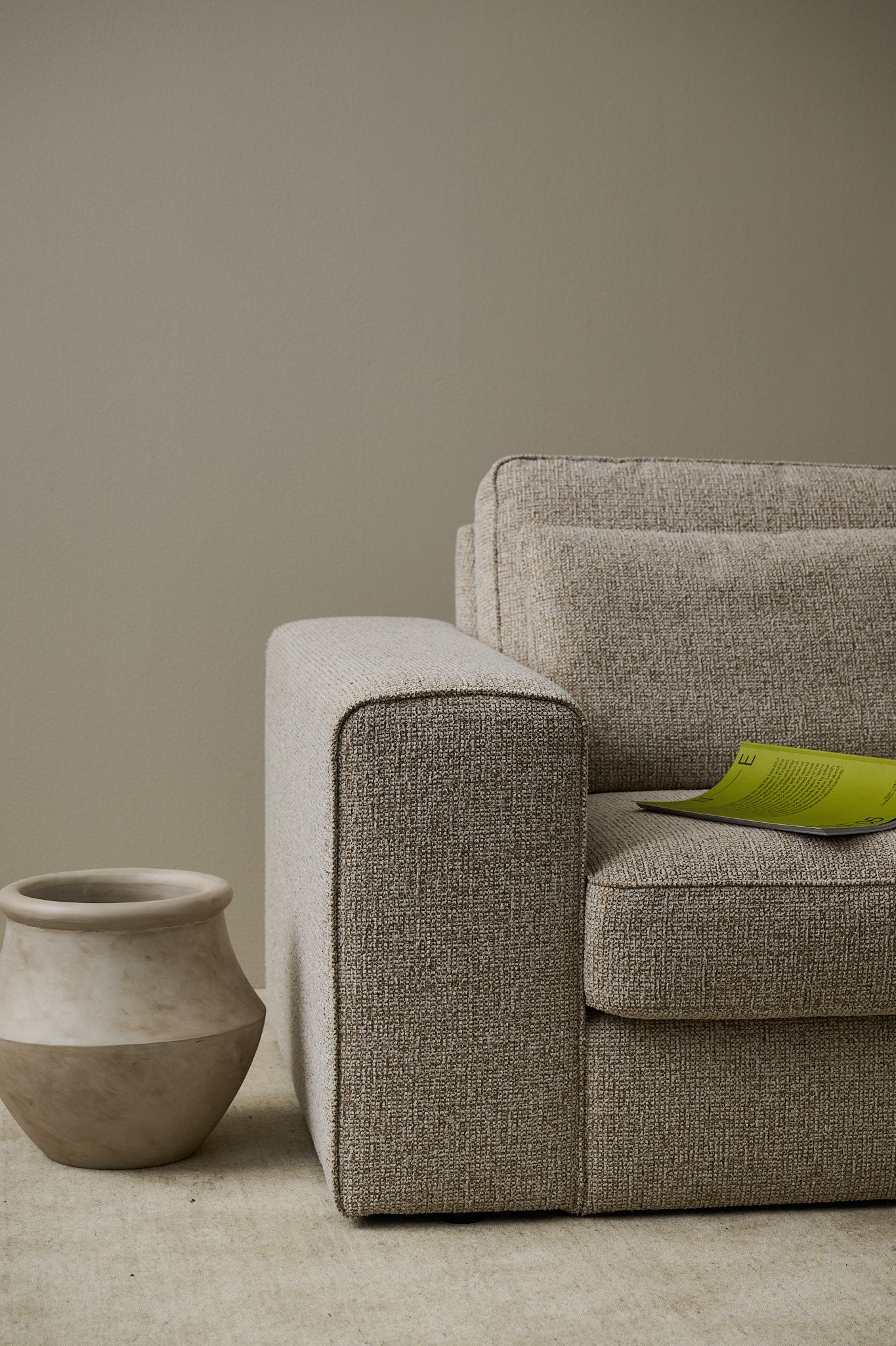 Close-up of a textured beige sofa with a green magazine, next to a two-toned vase on a light rug.