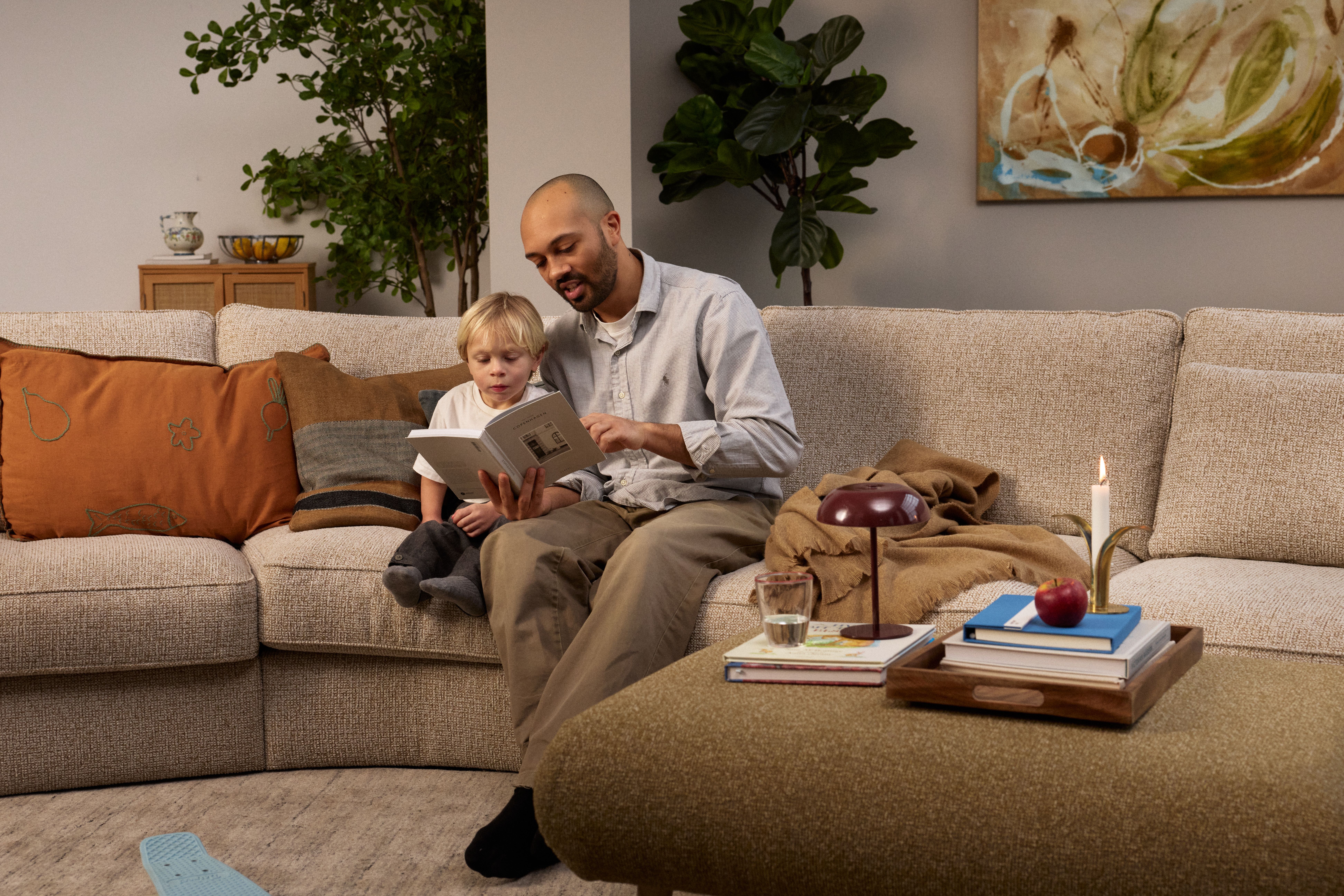 A father and son read a book together on a sofa in a cozy living room.