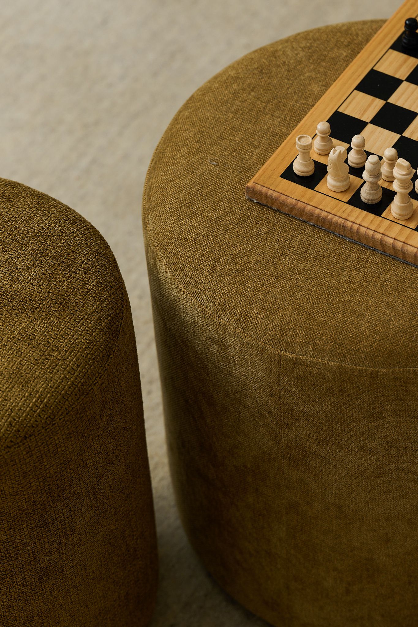 Two olive green fabric ottomans, one with a chessboard and white pieces.