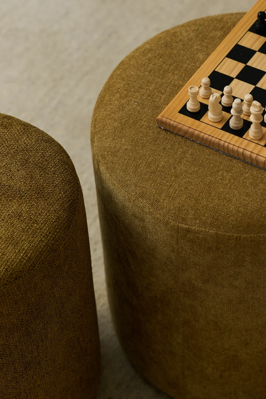 Two olive green fabric ottomans, one with a chessboard and white pieces.