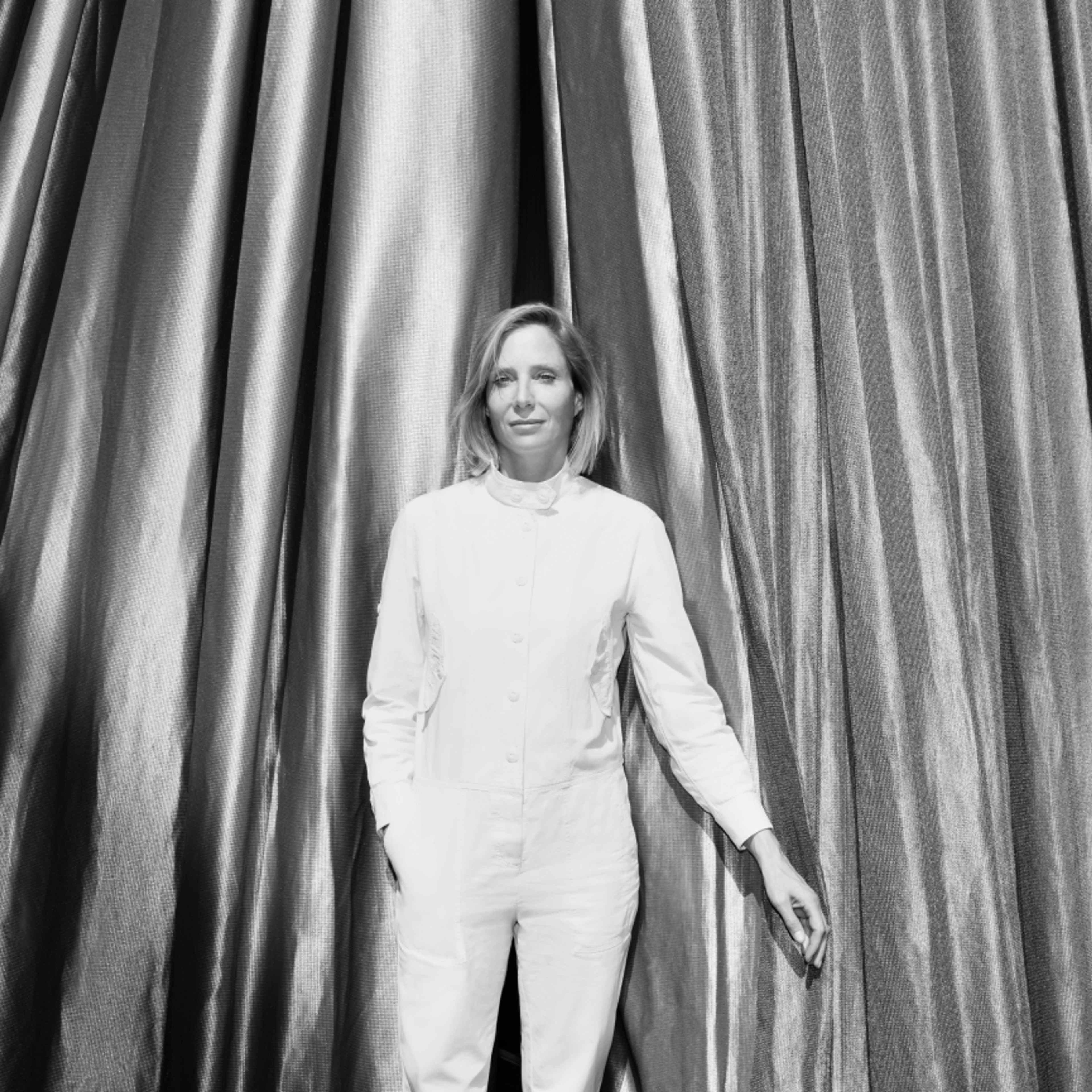 Black-and-white portrait of Dr. Bettina Kames, director of the Berlin-based art foundation LAS, standing in front of curtains.