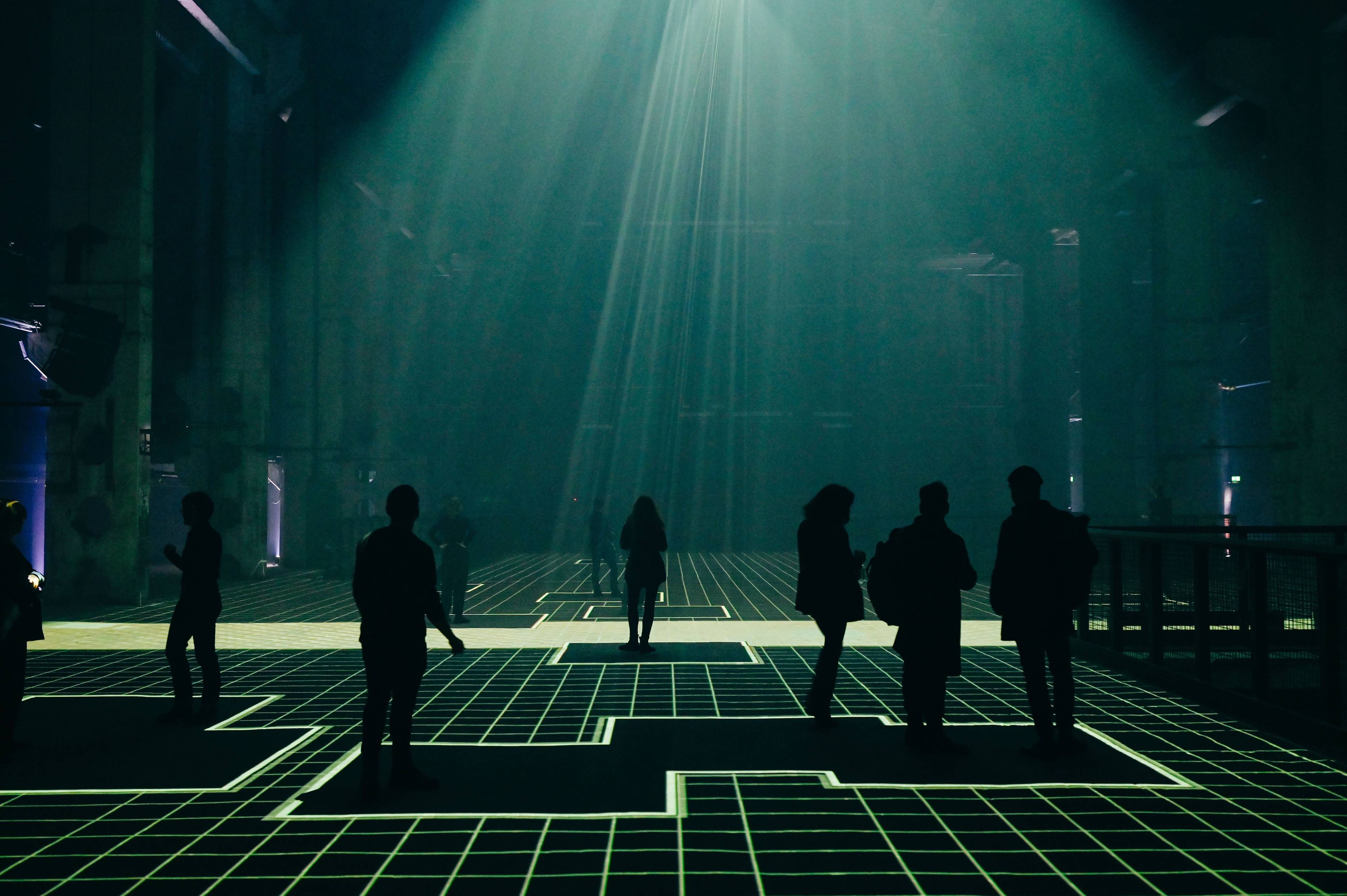 Silhouetted figures standing atop AI-generated grid patterns in a cavernous art space.