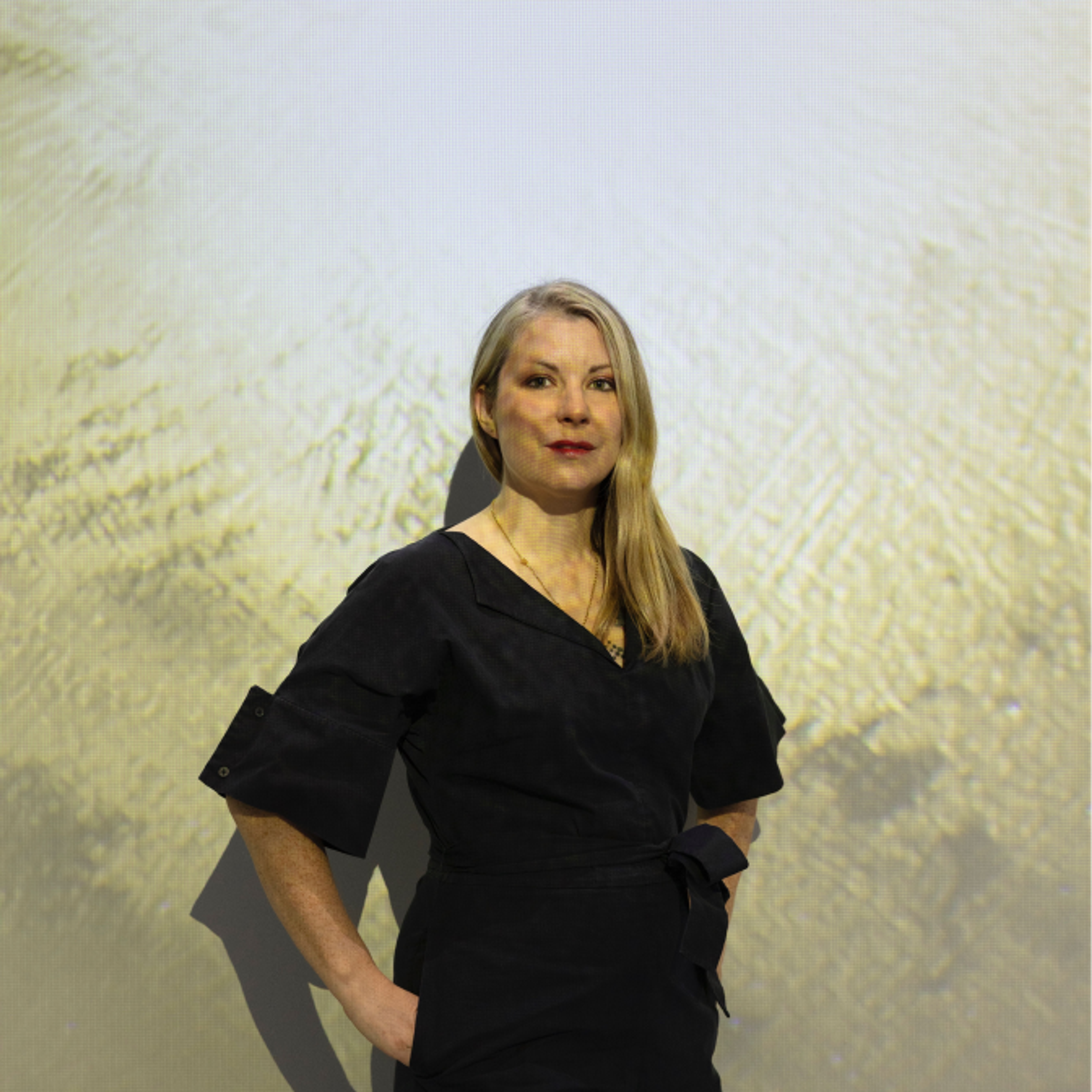 Quantum artist Libby Heaney standing against a wall with one of her projections.