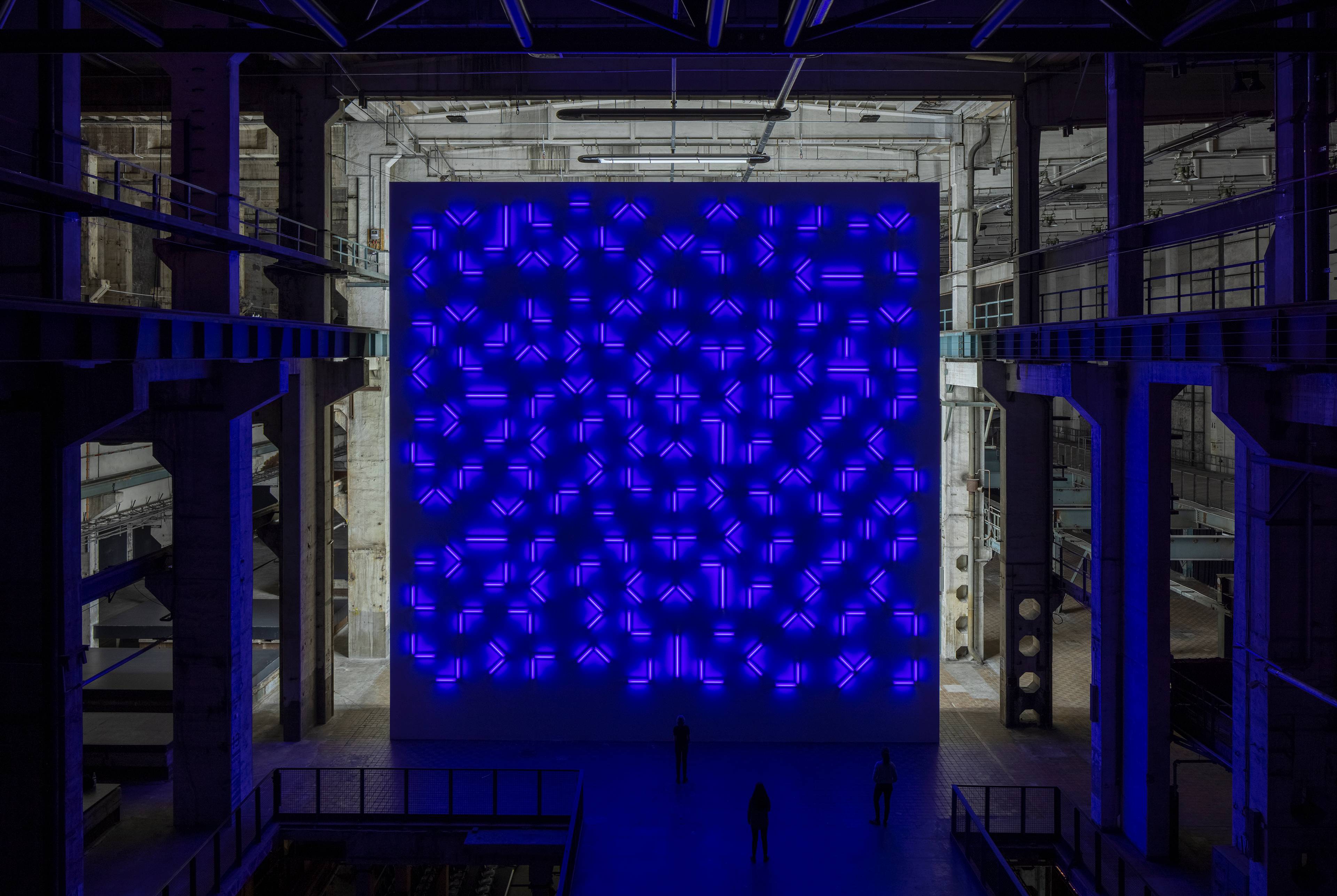 Eine riesige Wand aus gemusterten Leuchtstoffröhren leuchtet in einem violett-blauen Farbton im Kraftwerk Berlin