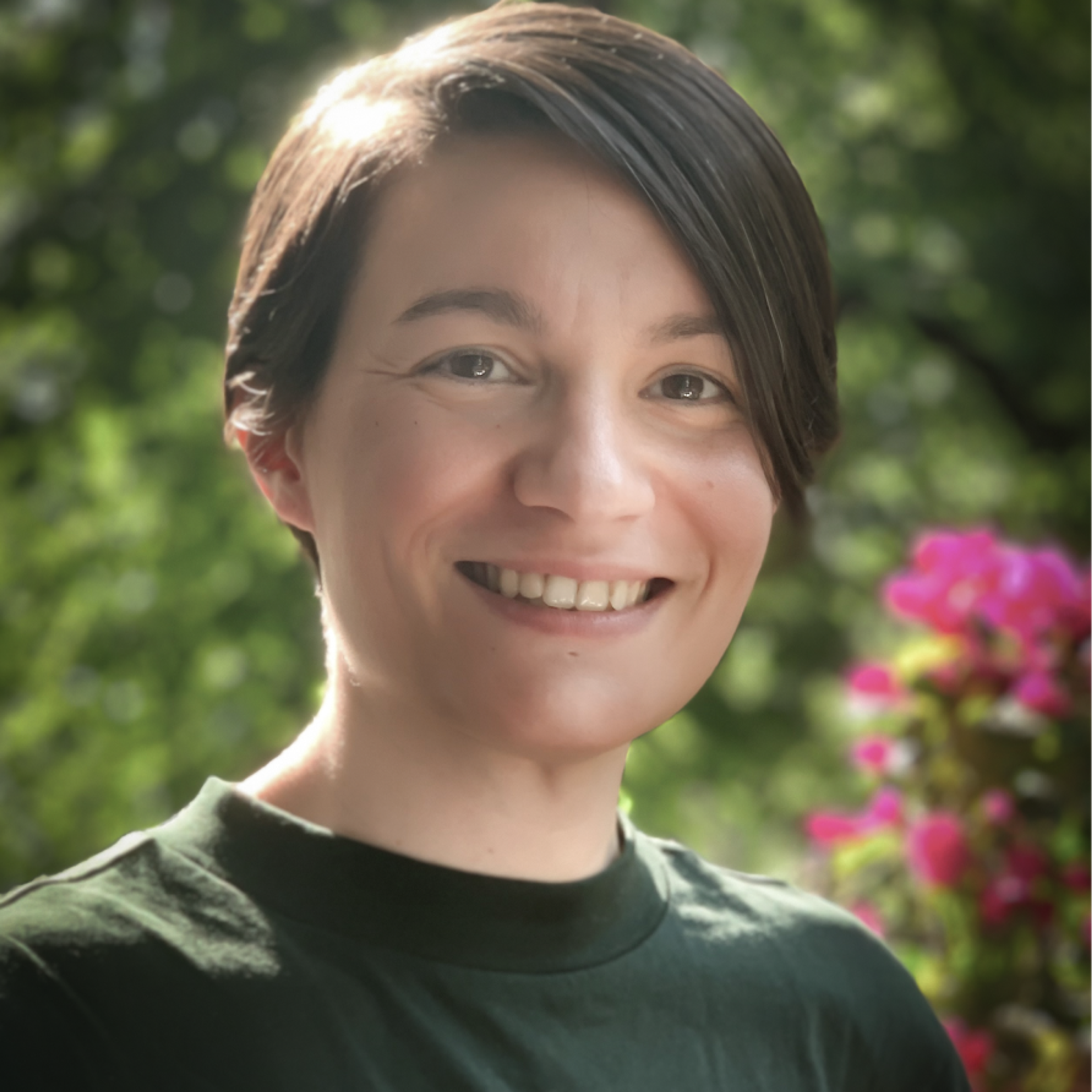 Porträt der Quantenforscherin Anna Pappa in einer Gartenlandschaft mit rosa Blumen.