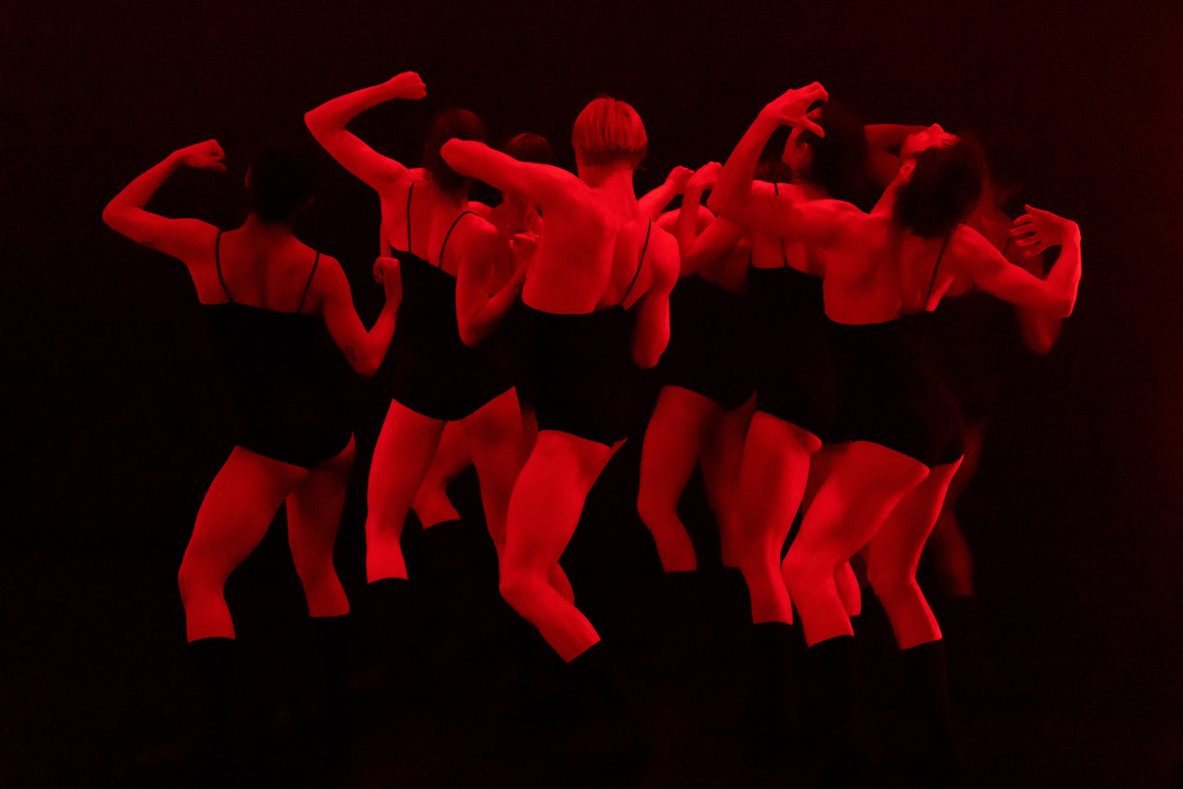 Group of dancers with backs turned and arms curling upward in a 2022 performance of Wet.