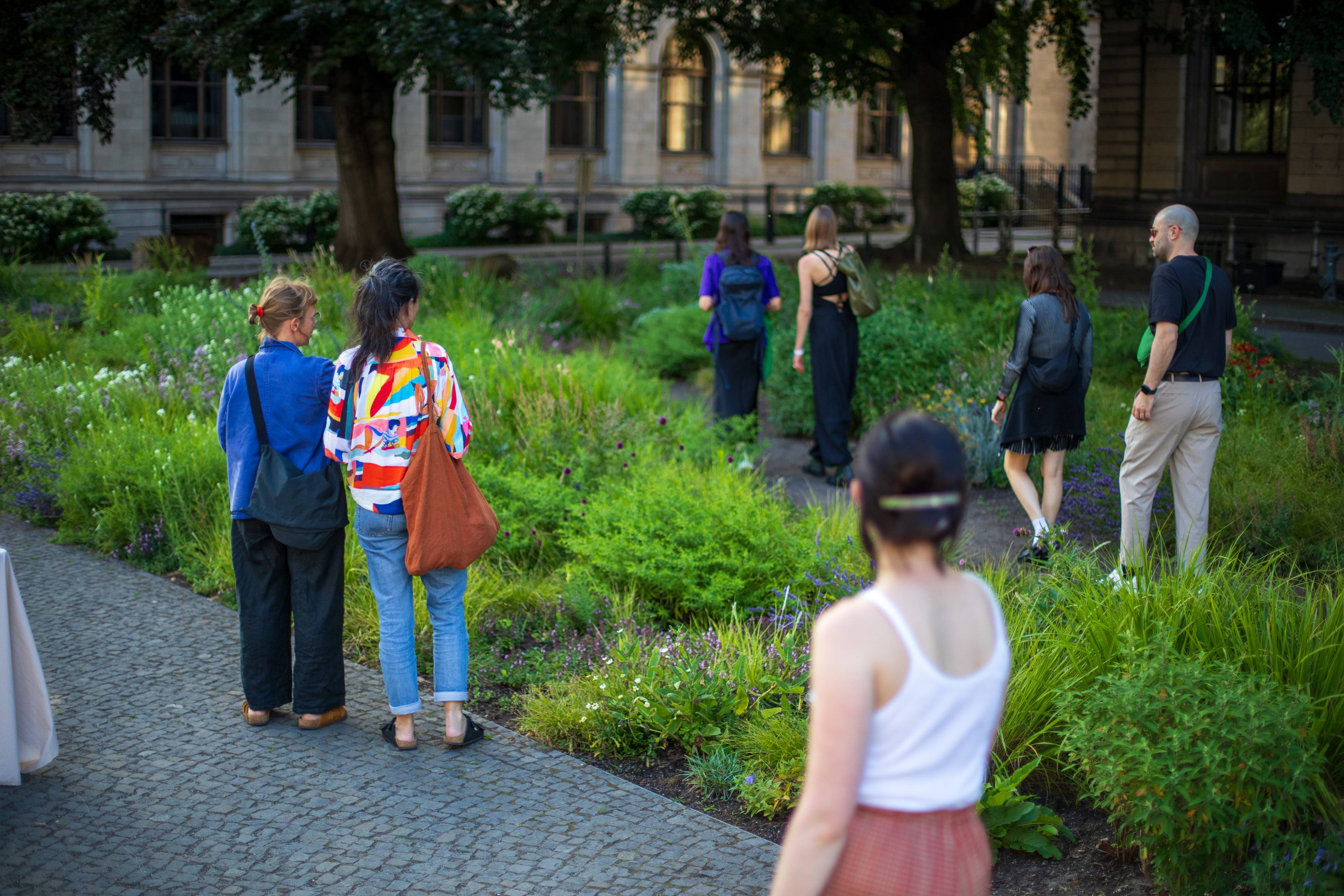 Visitors walk through and observe the Pollinator Pathmaker at the Museum für Naturkunde Berlin surrounded by mature trees.