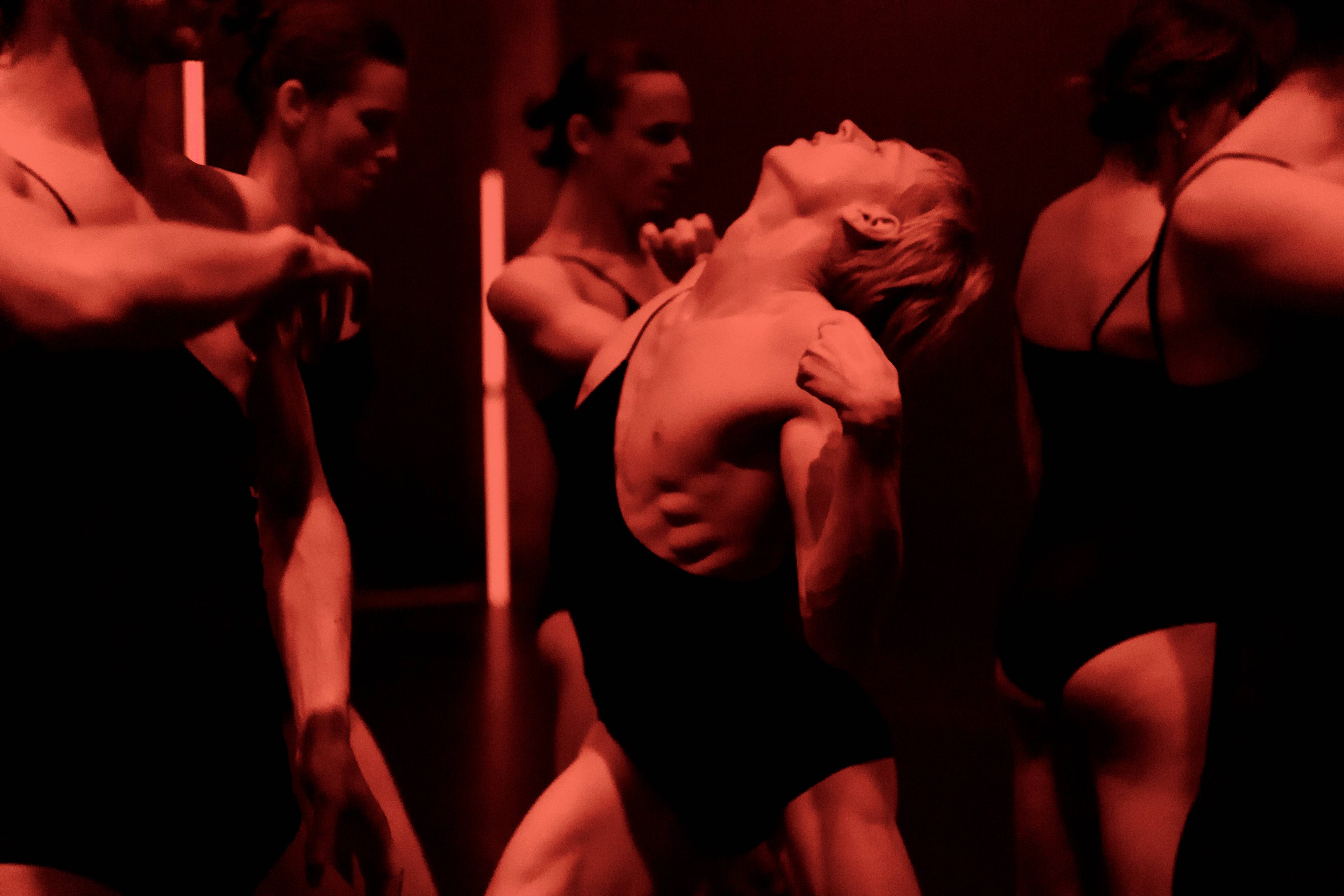 Action shot of dancers from L-E-V dance company bathed in red light.