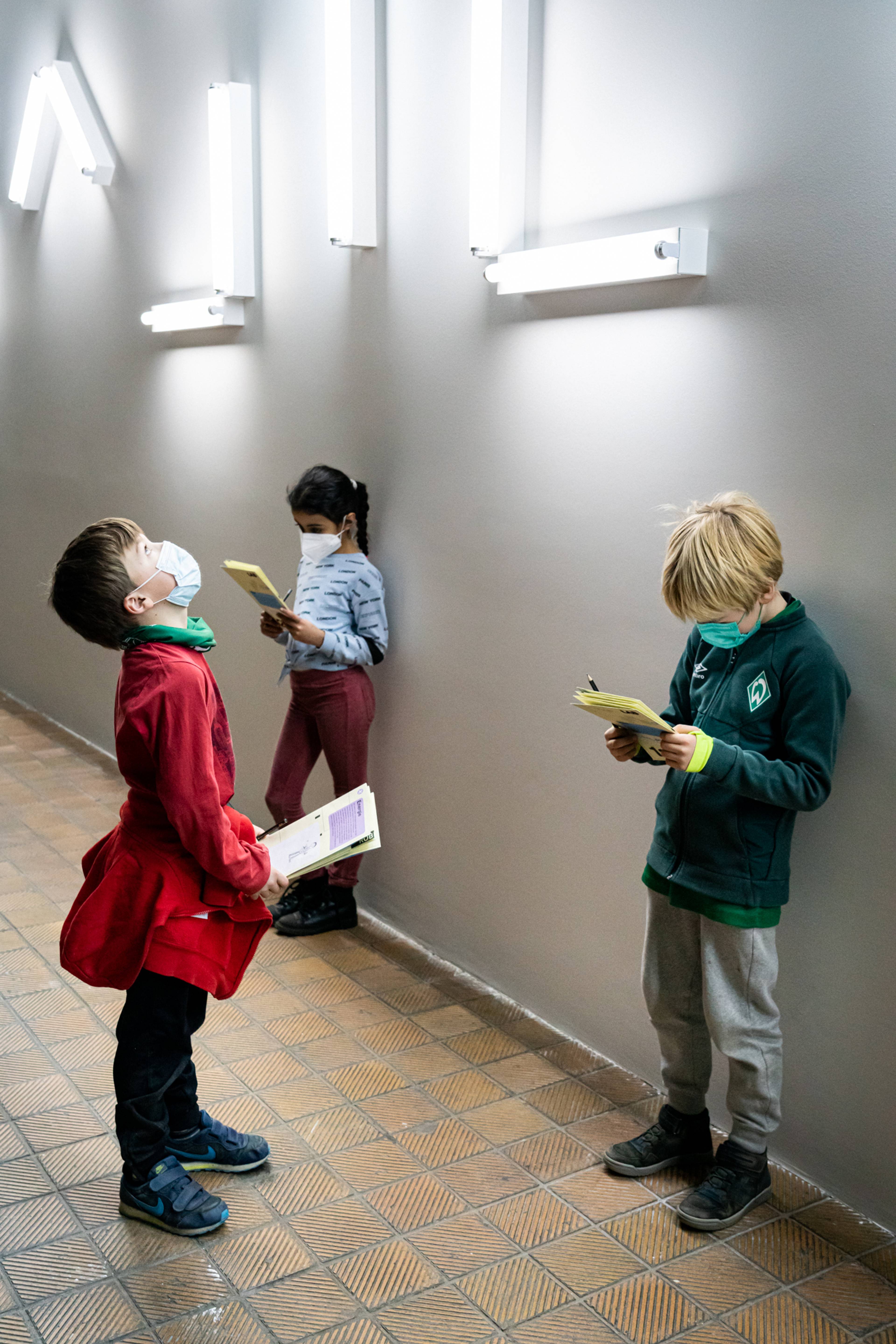 Drei Schulkinder mit Covid-Masken lesen vor einer von Robert Irwin entworfenen Lichtinstallation Unterrichtsmaterial.