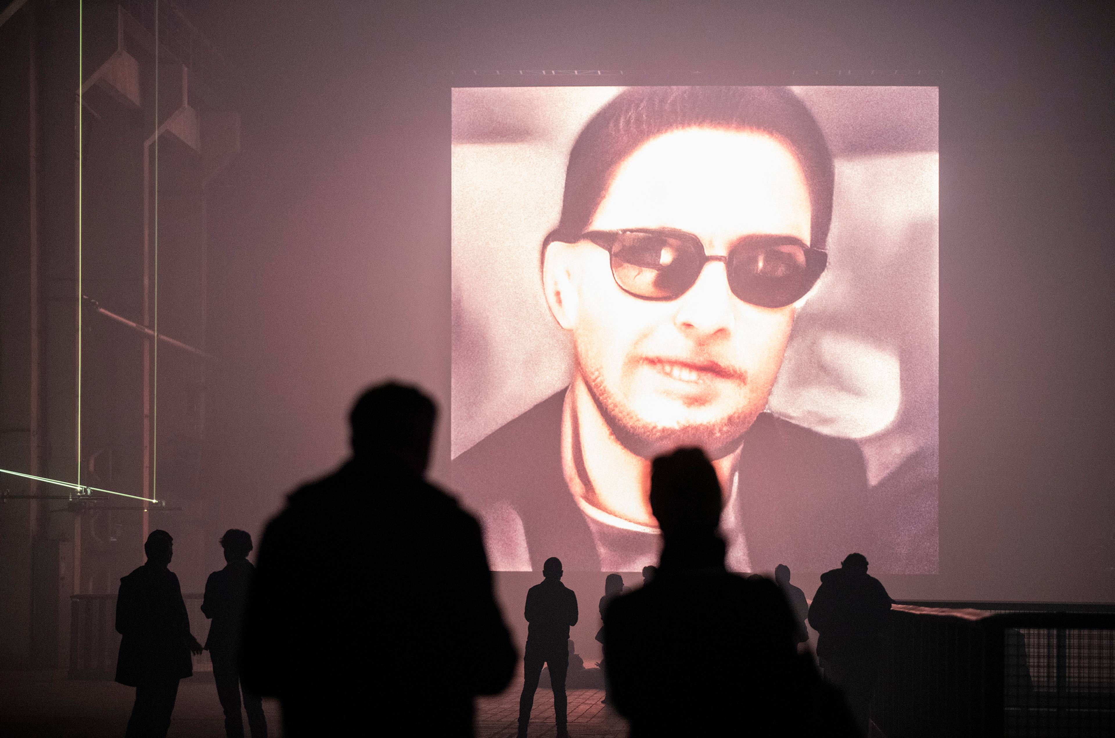 Large-scale AI data painting of a bearded man in sunglasses displayed on an LED wall in Kraftwerk Berlin.