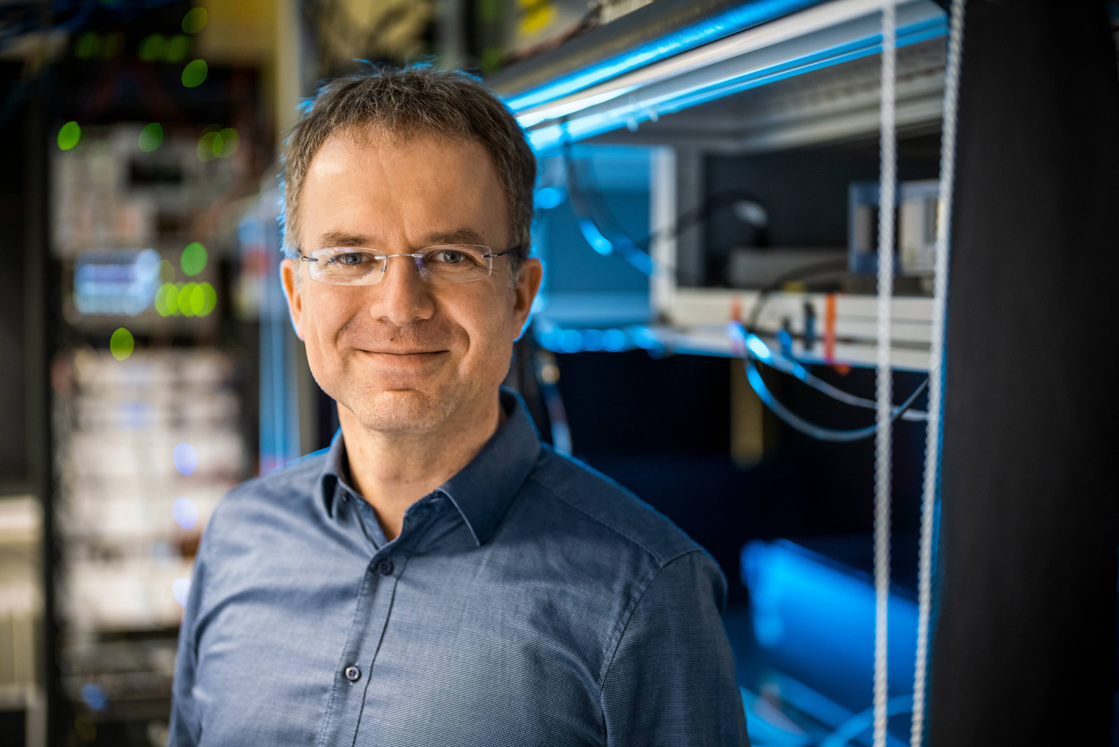 Smiling portrait of experimental physics professor Christian Ospelkaus standing in front of a large computer.
