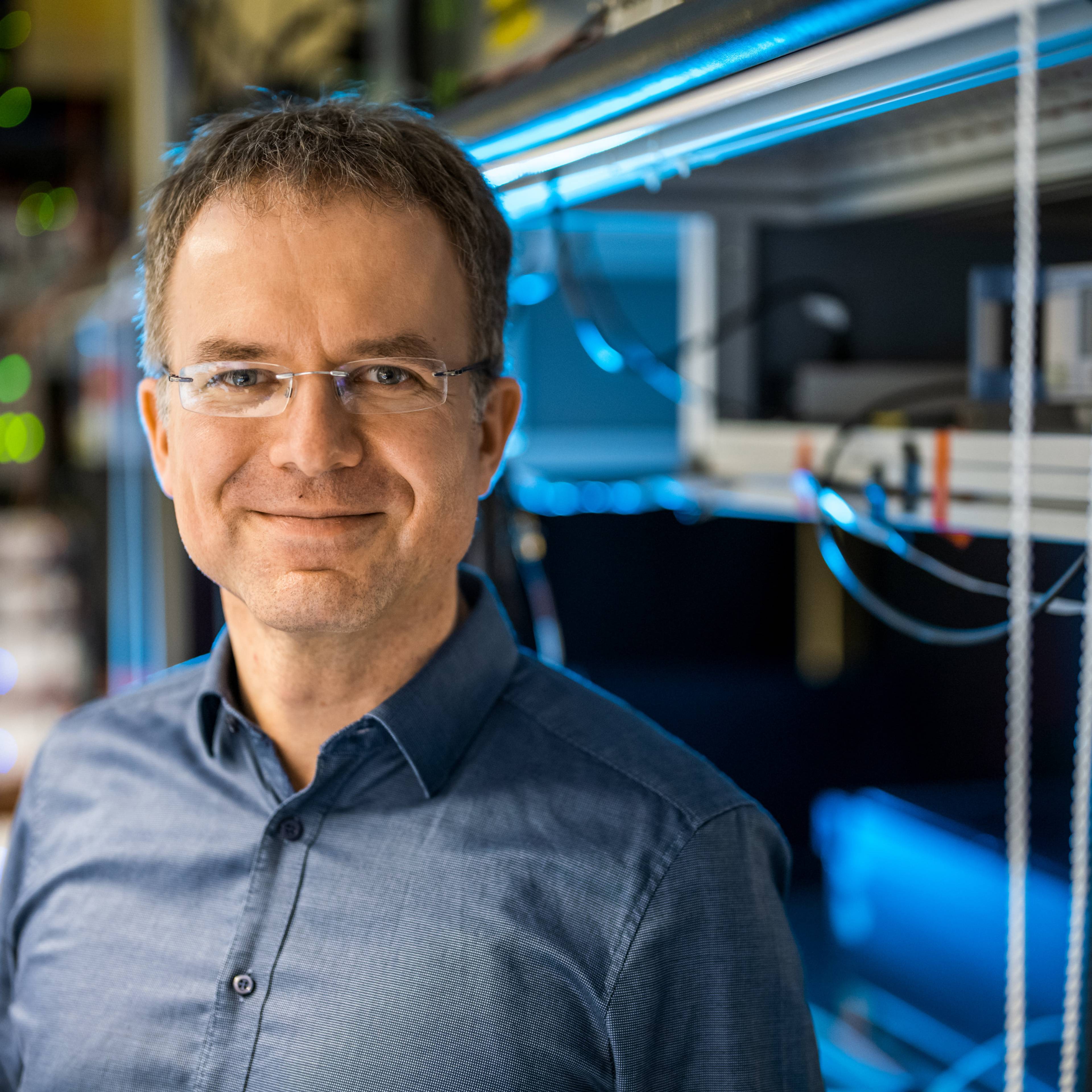 Smiling portrait of experimental physics professor Christian Ospelkaus standing in front of a large computer.