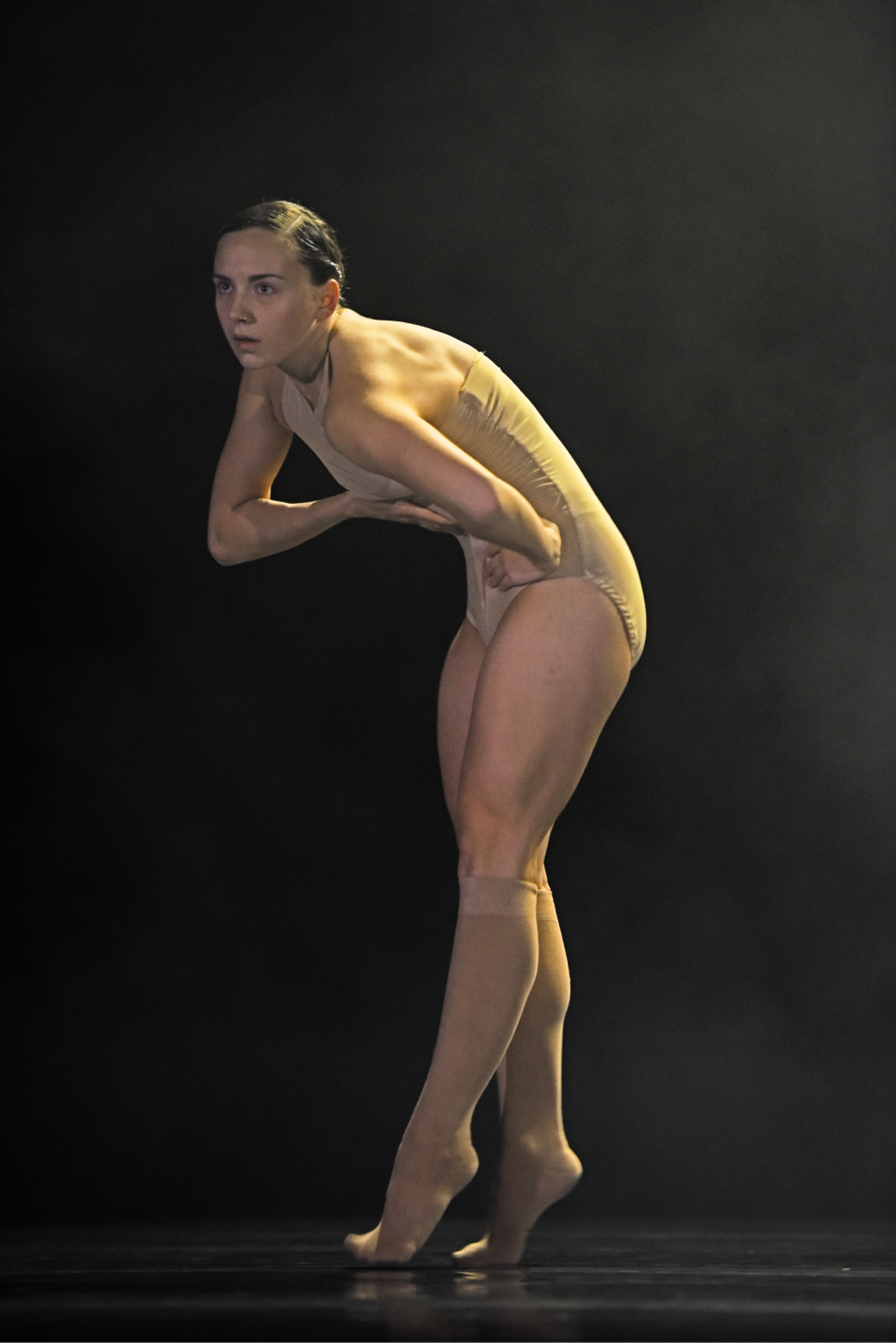 Woman dancer from the tanzmainz ensemble crosses her legs and arms and bends over in the production Soul Chain.