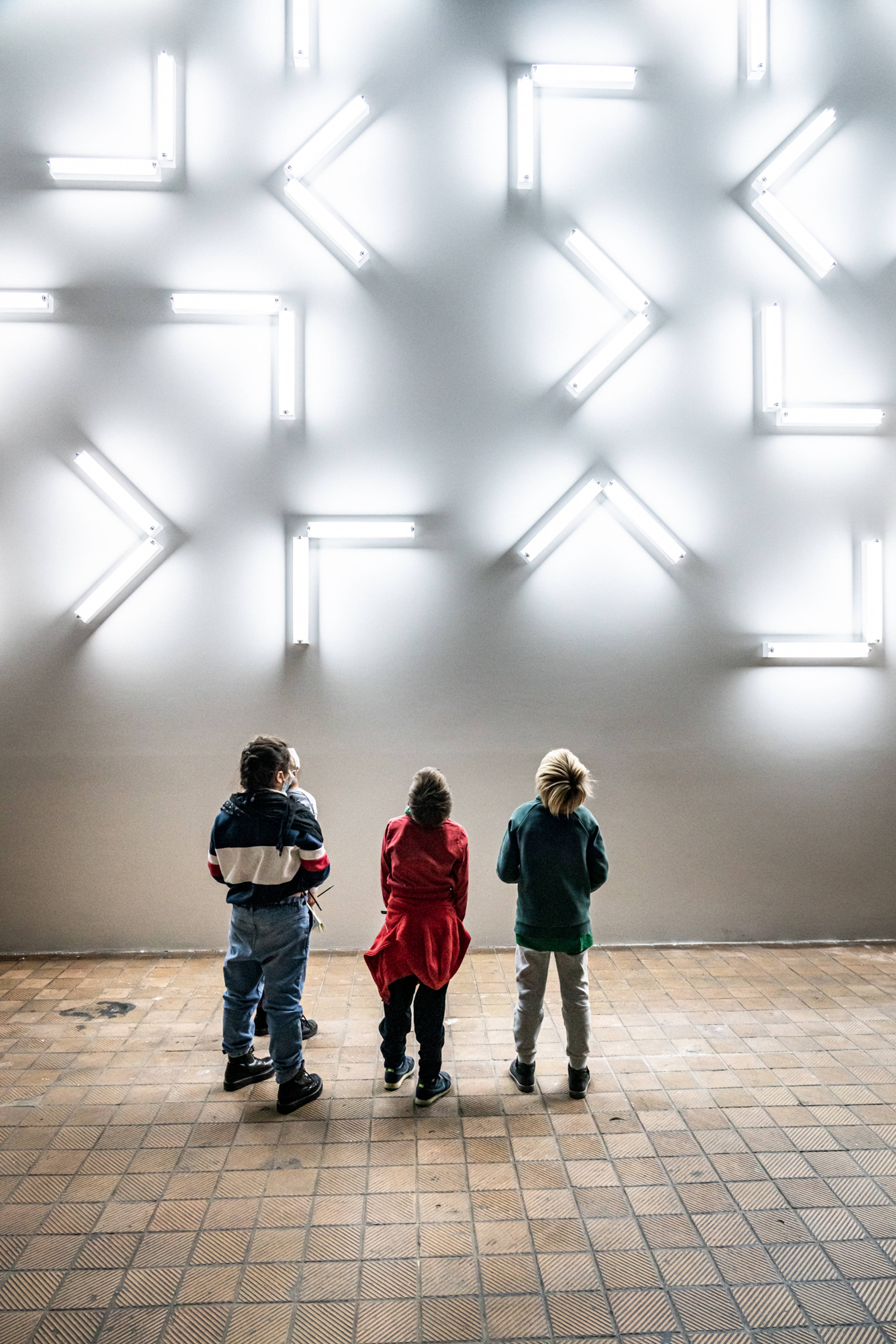 Vier Schulkinder blicken auf die weißen Lichtbalken, die Robert Irwins Kunstwerk Light and Space im Kraftwerk Berlin bilden.