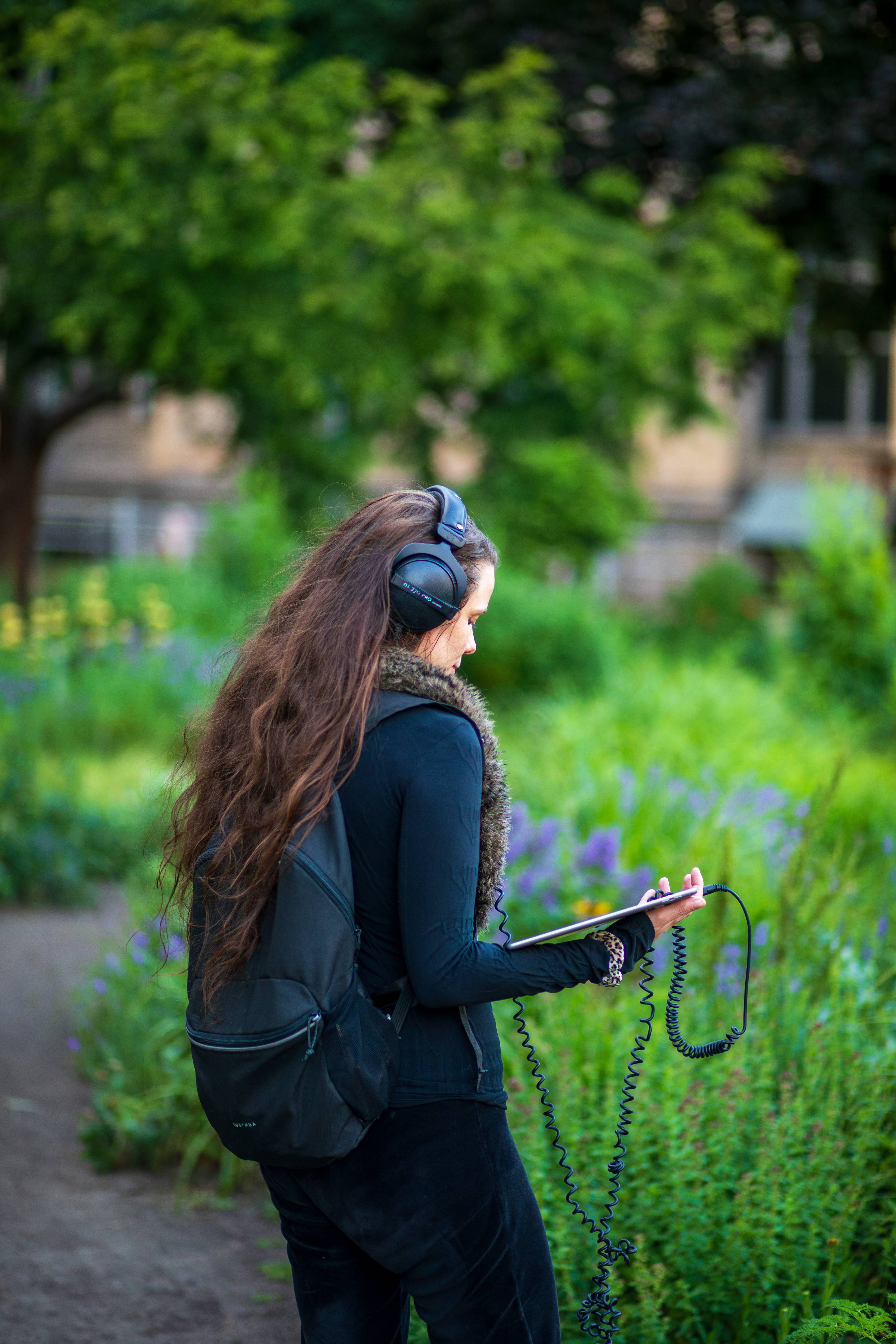 A visitor wearing headphones listens to an audio work while standing among flowering plants inside Pollinator Pathmaker.