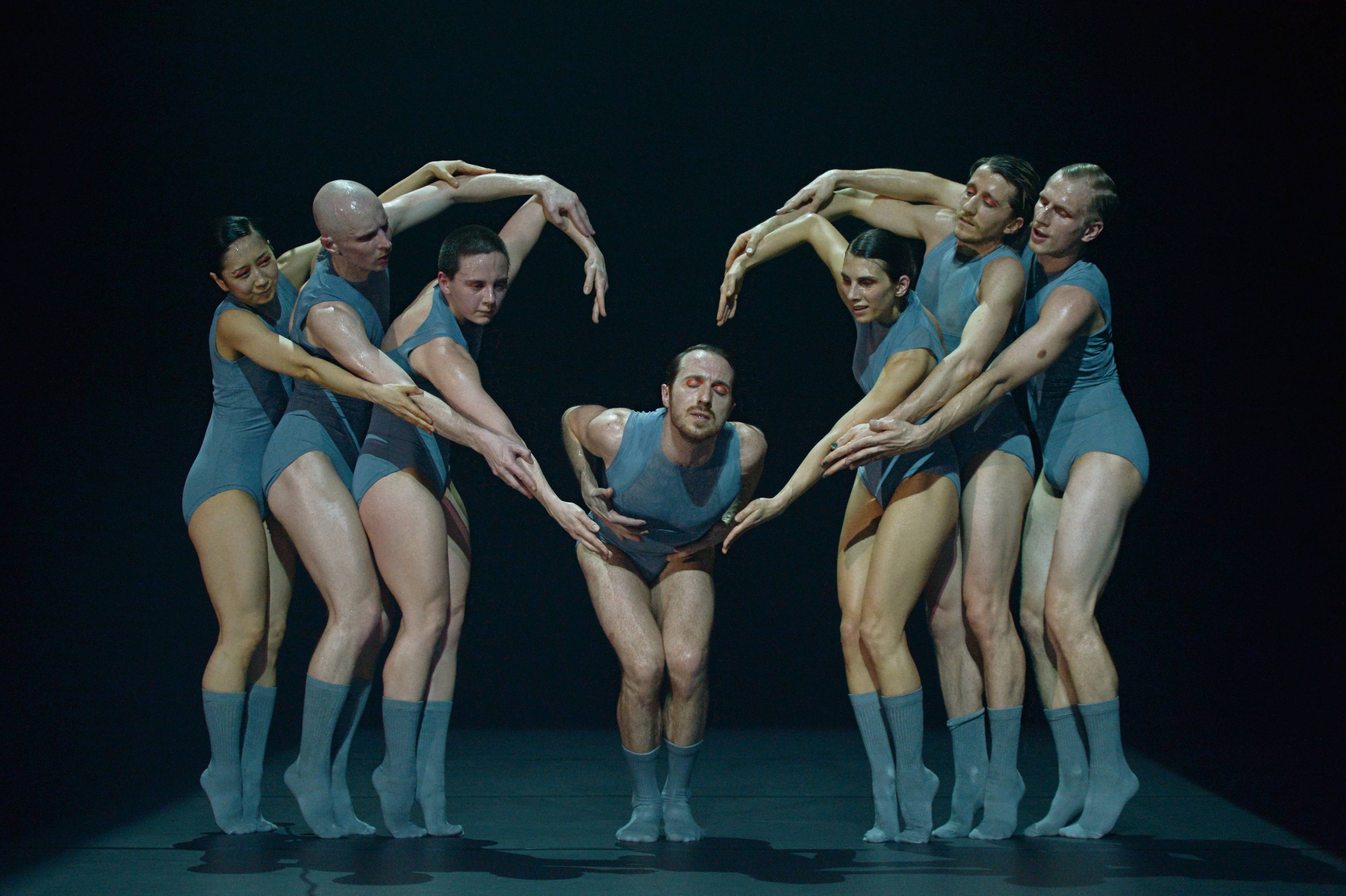 Male dancer bends over as six dancers surround him with arms forming a heart shape in the tanzmainz production Promise.