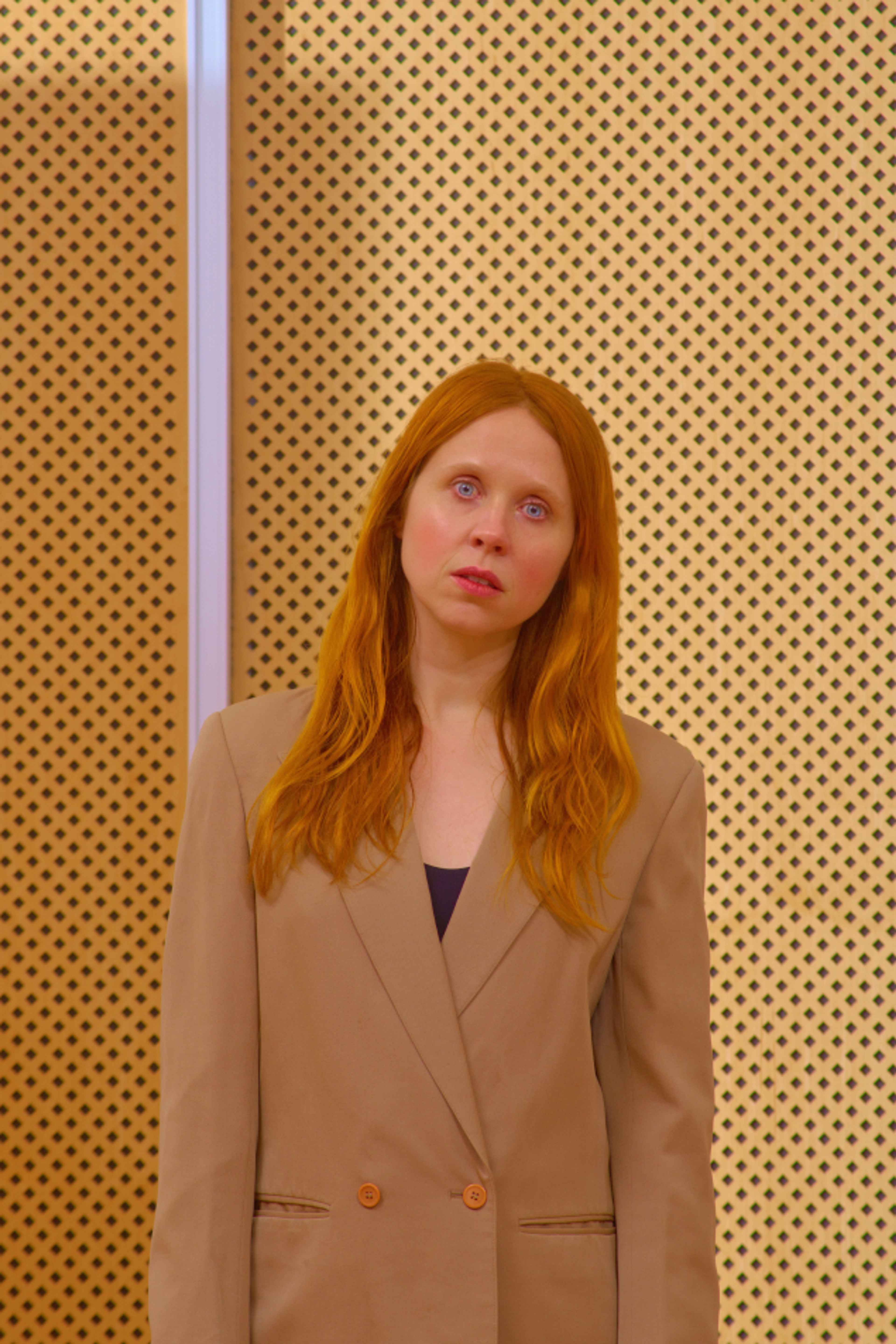 Portrait of Holly Herndon with head slightly tilted, against a yellow background with black dots.