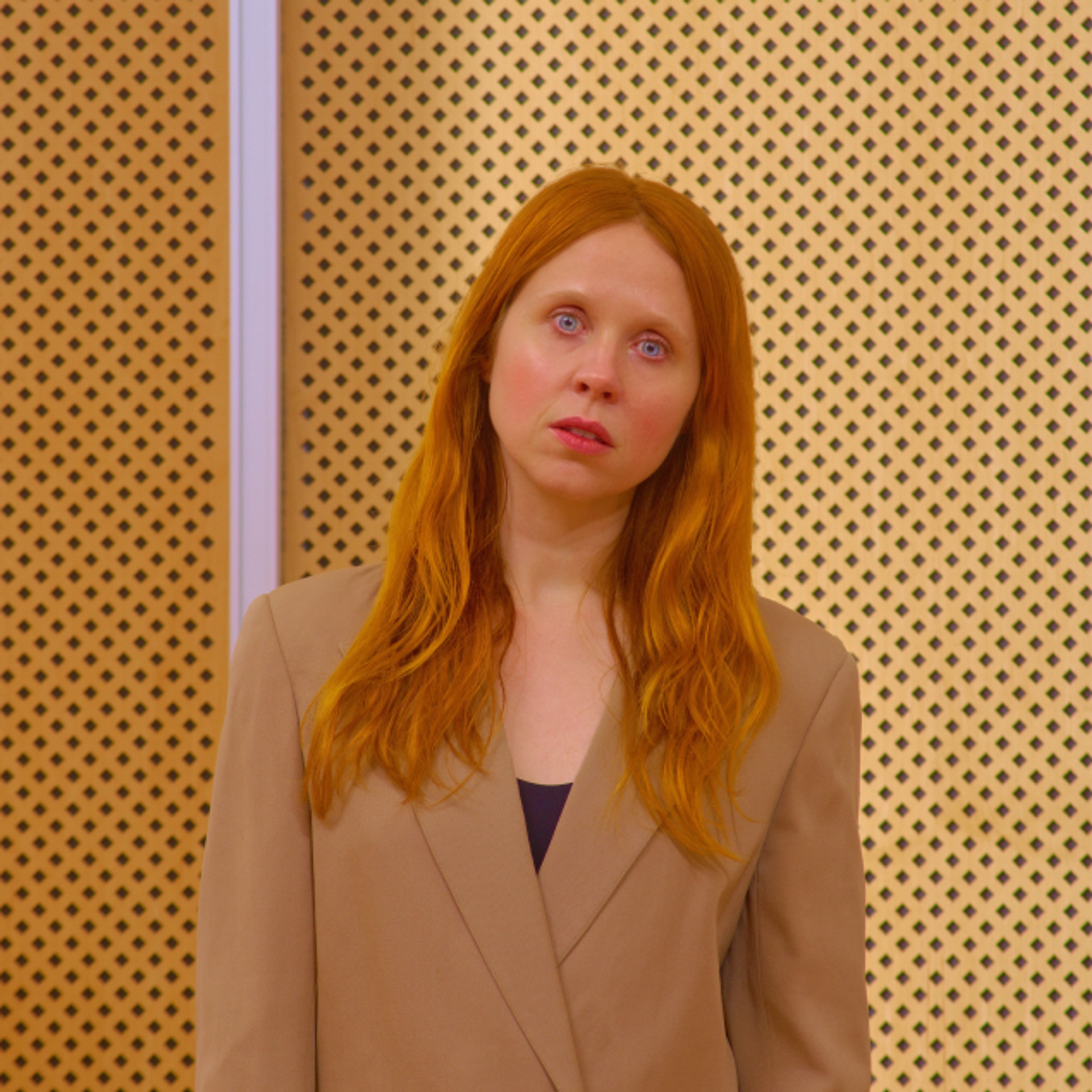 Portrait of Holly Herndon with head slightly tilted, against a yellow background with black dots.