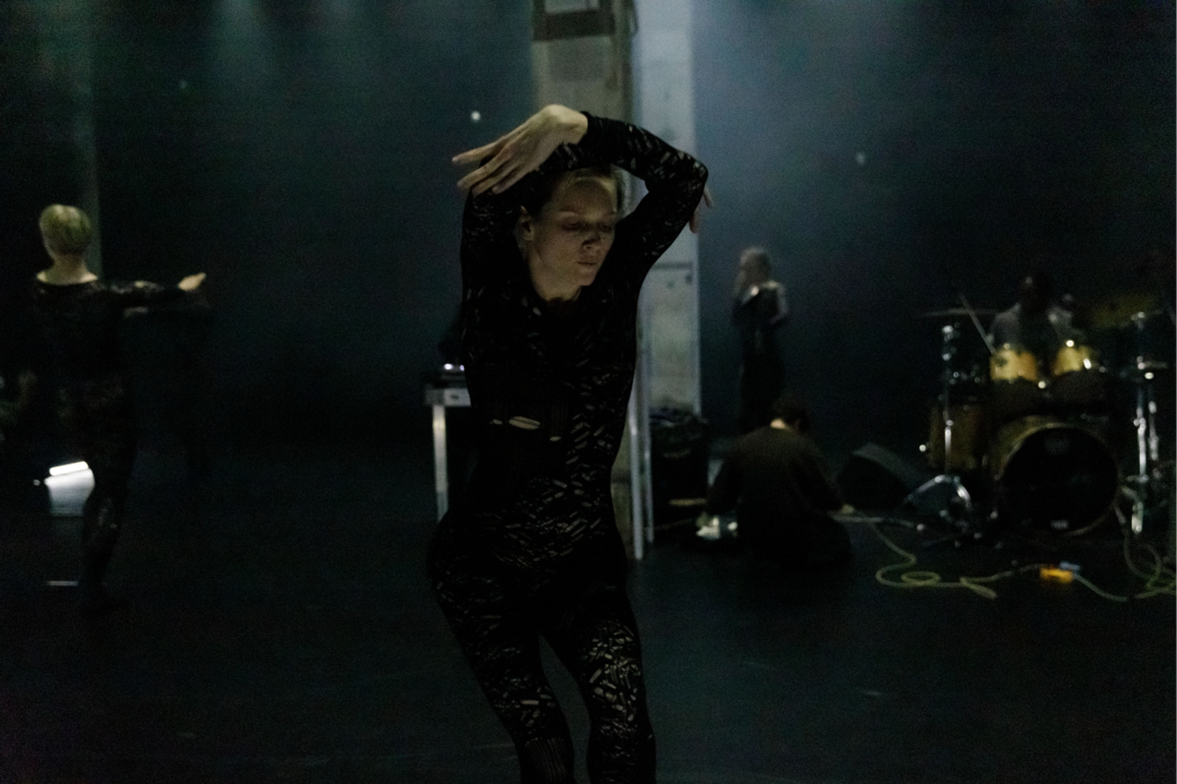 Woman in black outfit dancing with hands crossed above her head.