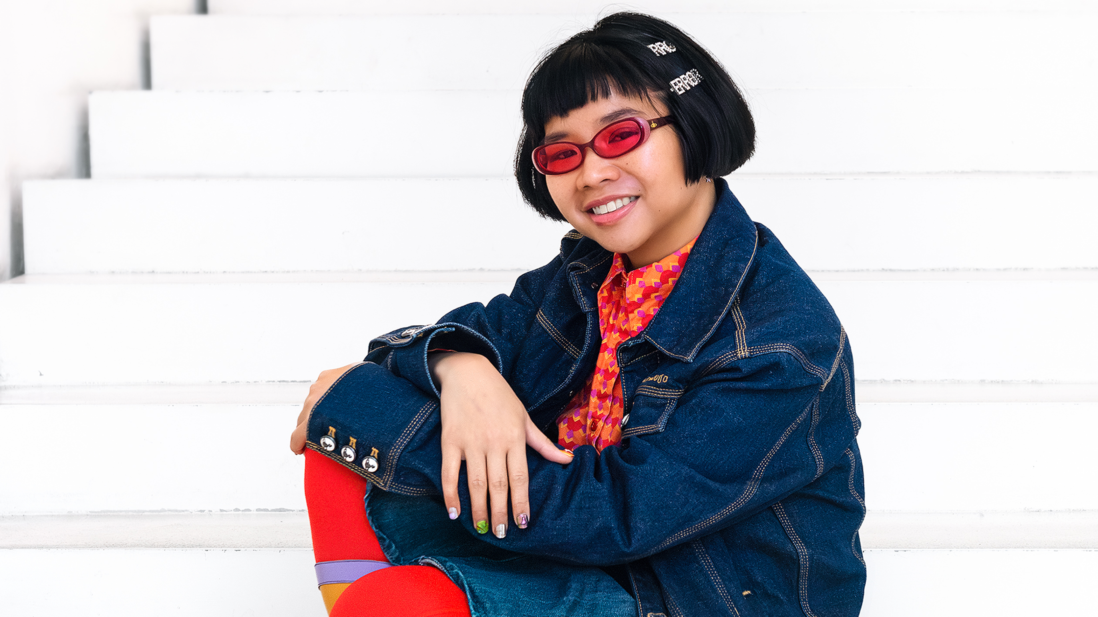 Red-and-black illustration featuring a cloaked central figure, stylised faces, skulls and dense abstract patterns creating a dramatic, surreal atmosphere.