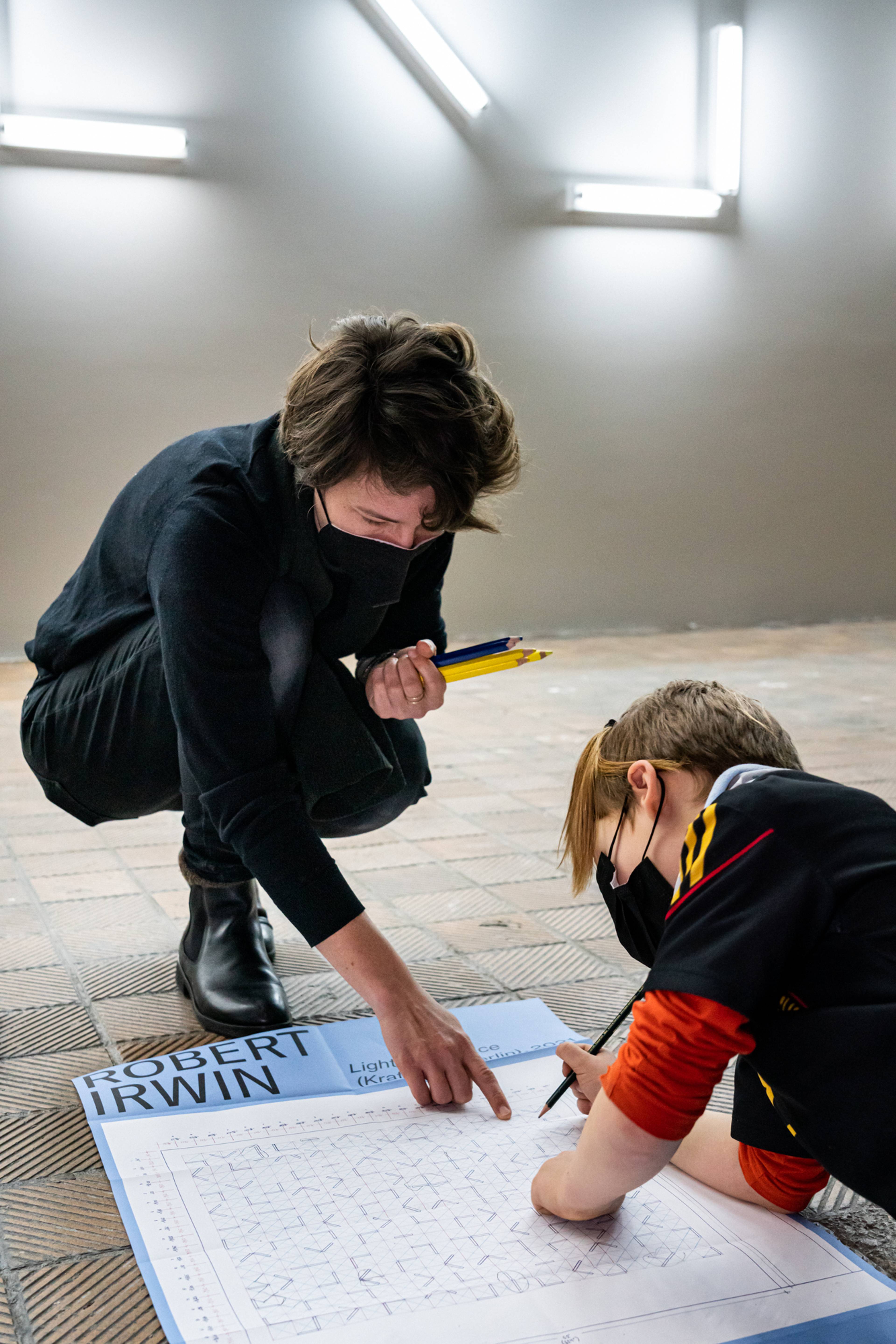 Eine Kunstpädagogin beugt sich hinunter, um einem Kind beim Ausfüllen eines Robert-Irwin-Arbeitsblatts zu helfen.