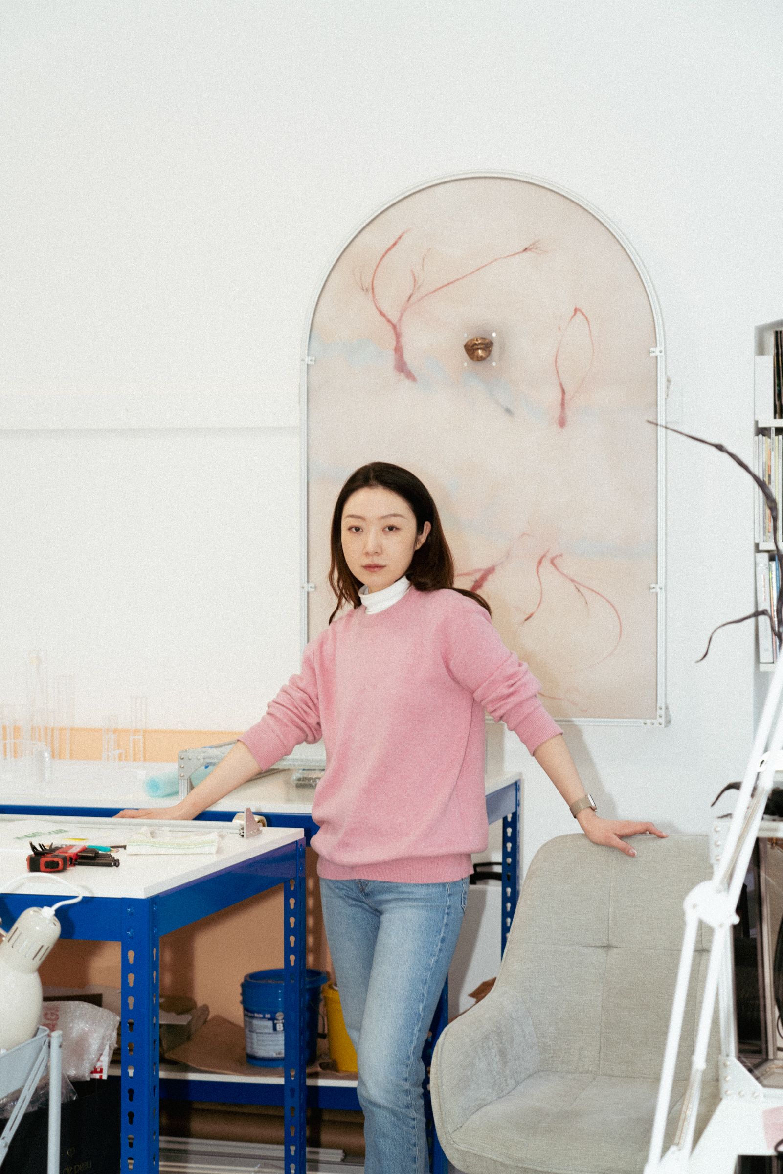 Portrait of a woman standing in her artist’s studio, surrounded by creative tools and artwork.