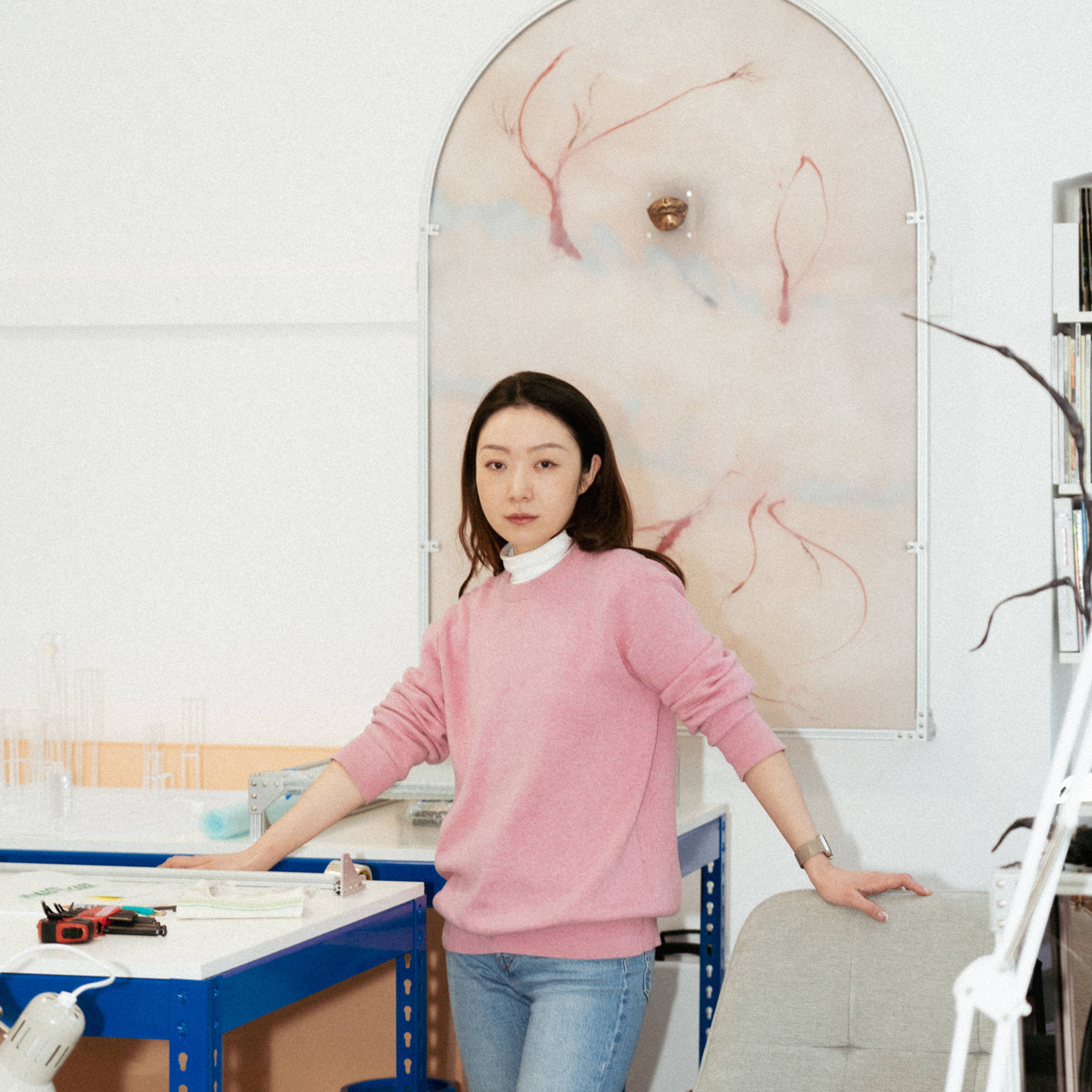 Portrait of a woman standing in her artist’s studio, surrounded by creative tools and artwork.