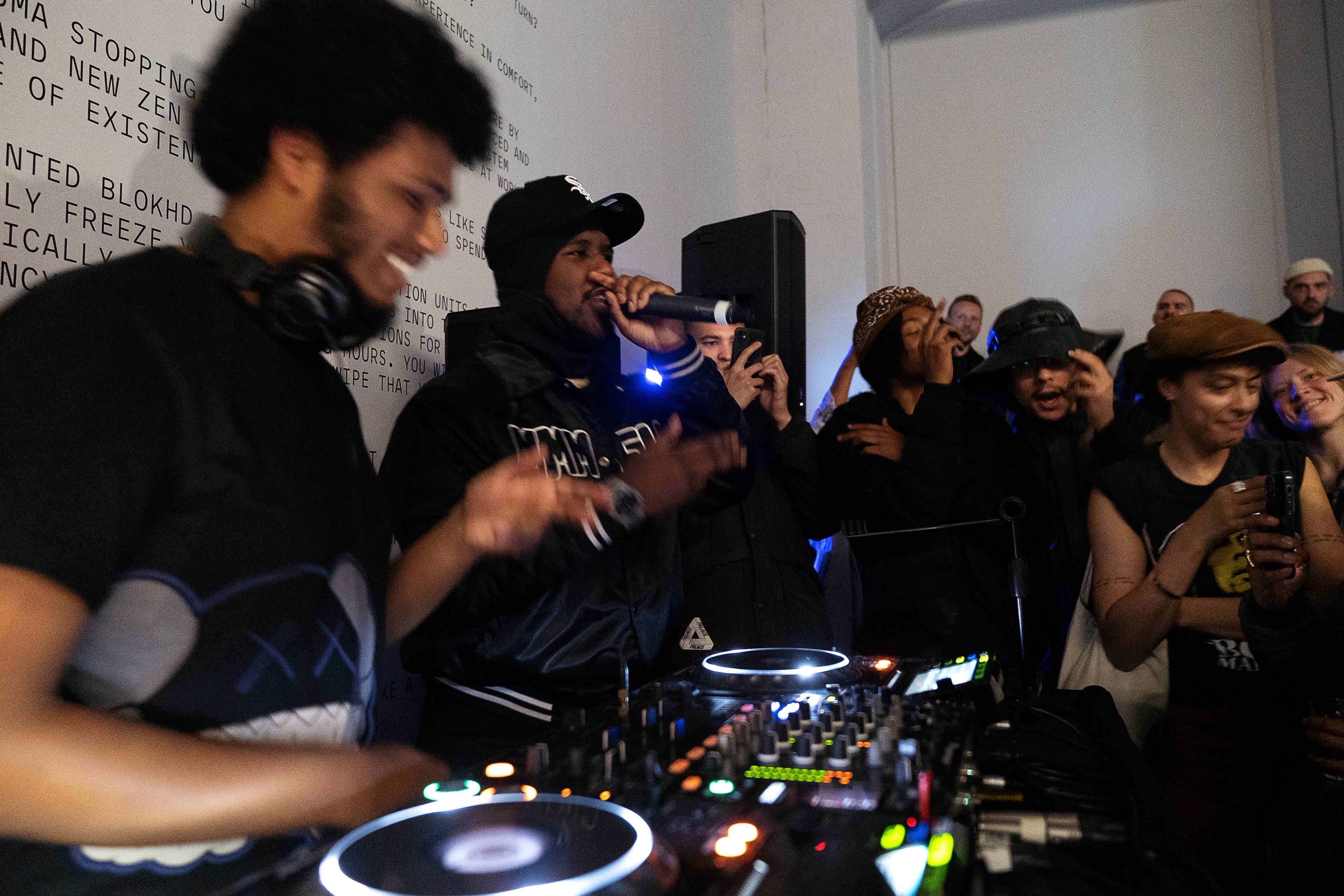 Ein DJ und ein Rapper treten bei einer gut besuchten Veranstaltung auf, das Publikum steht dicht gedrängt und genießt die Show.