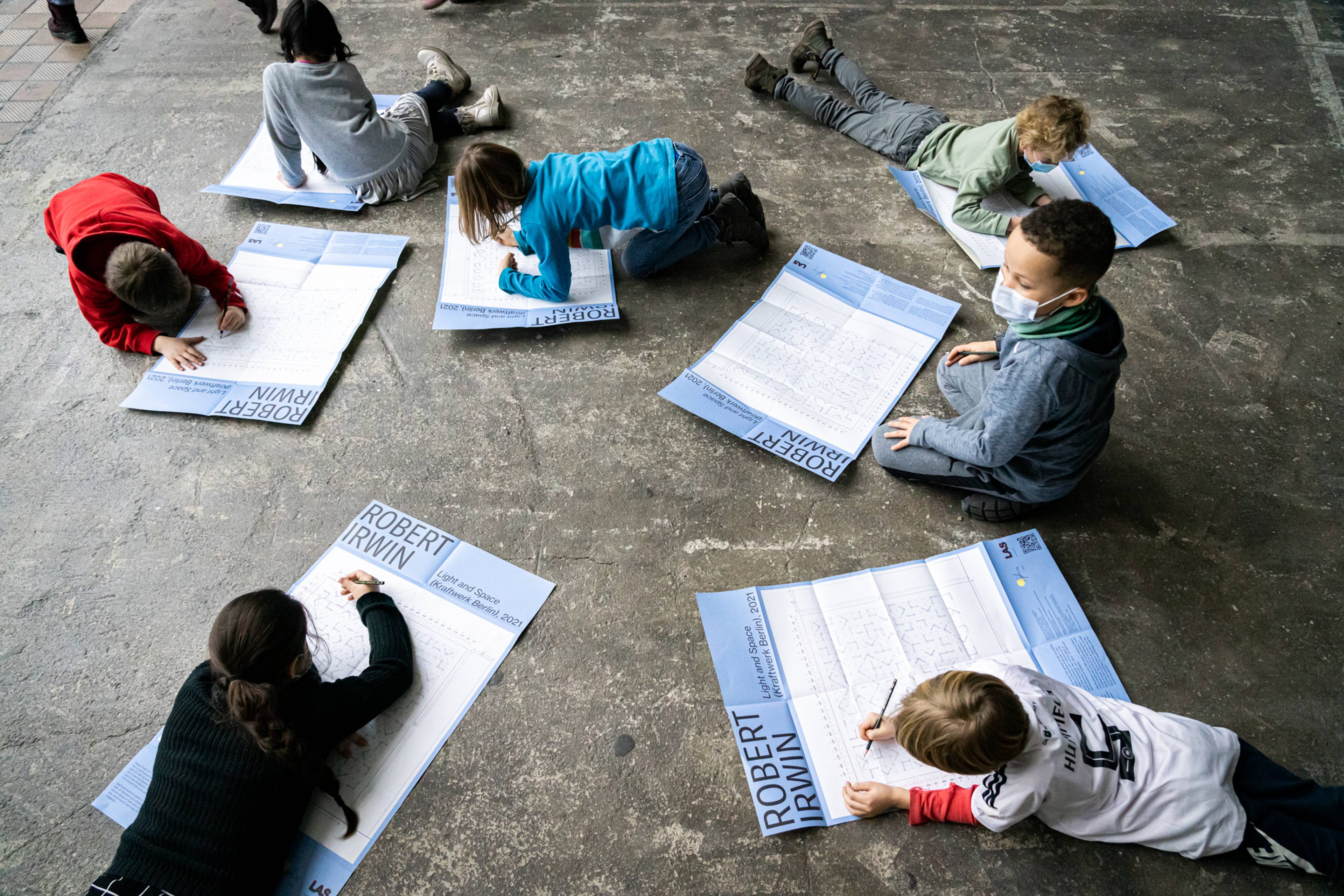 Eine Gruppe von Schulkindern in Covid-Masken liegt auf dem Boden und arbeitet an Robert-Irwin-Arbeitsblättern.