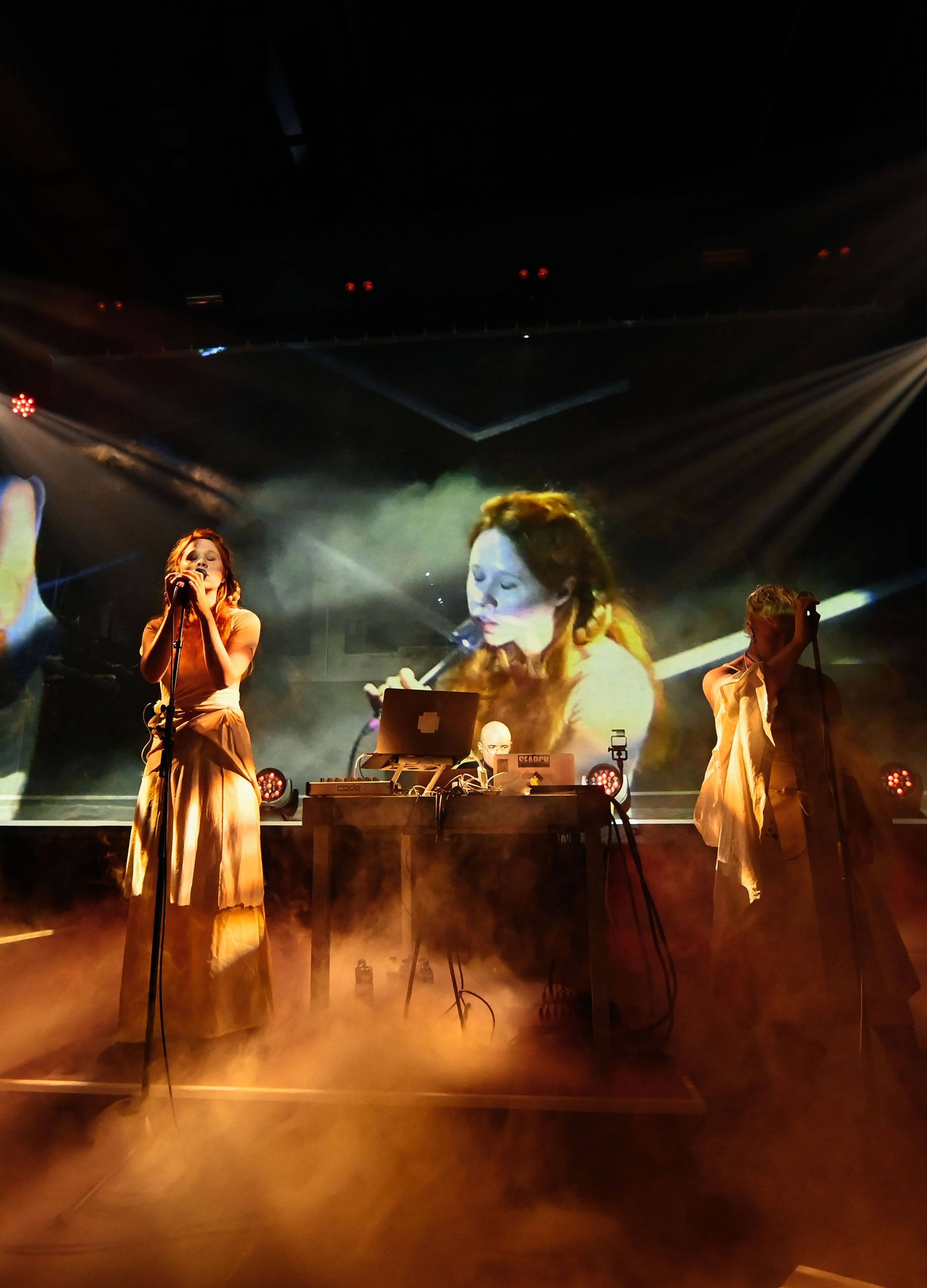 Vertical shot of Holly Herndon singing as her image is projected onto a screen behind her at Kraftwerk Berlin.