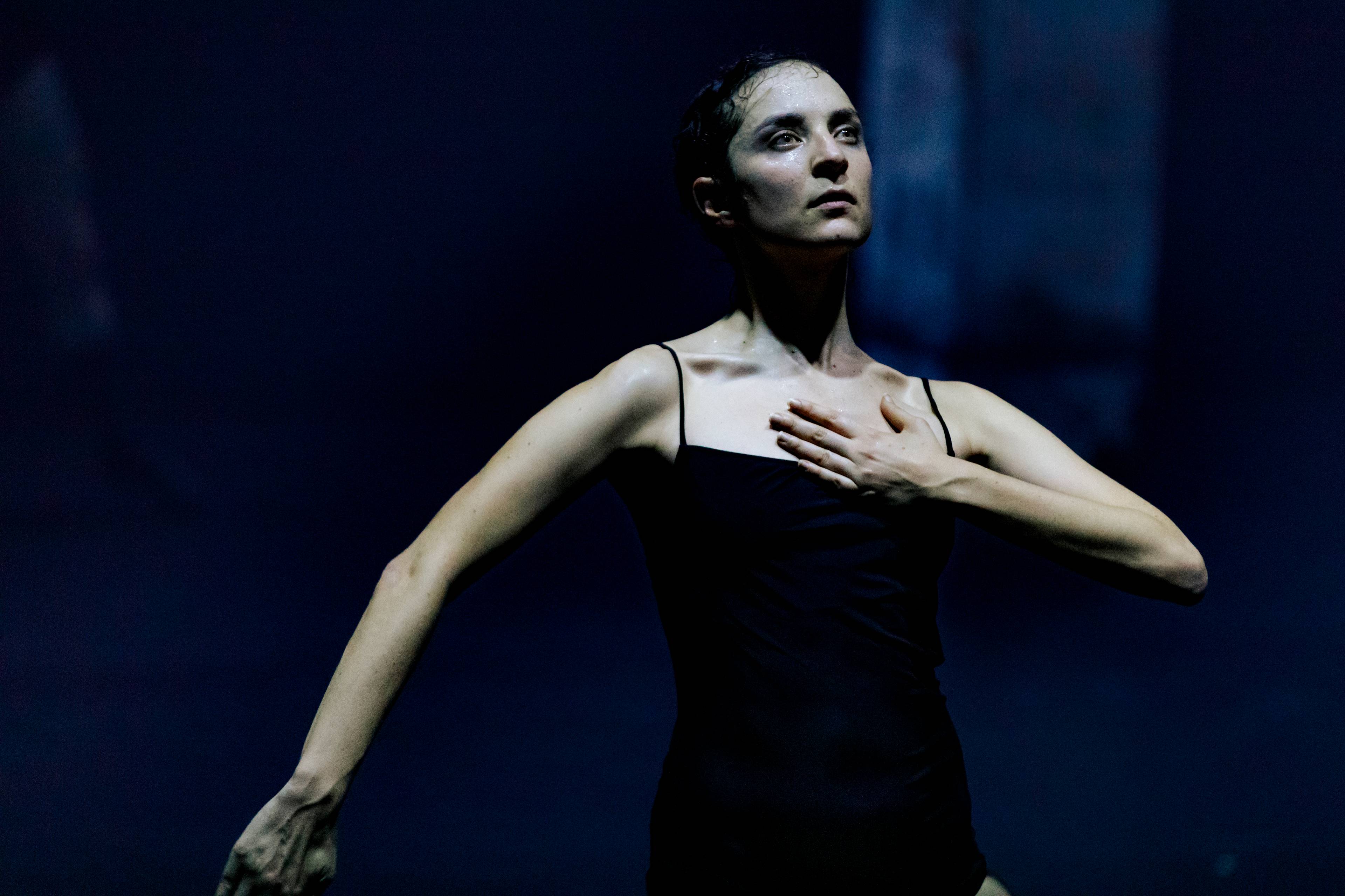 Woman dancer in black holds one hand to her chest during a performance of This Is Not a Love Show at Kraftwerk Berlin.