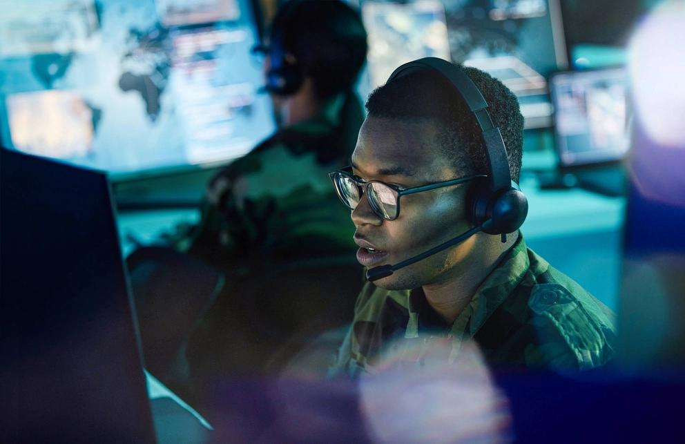Defence IT worker in a headset studies a monitor intensely