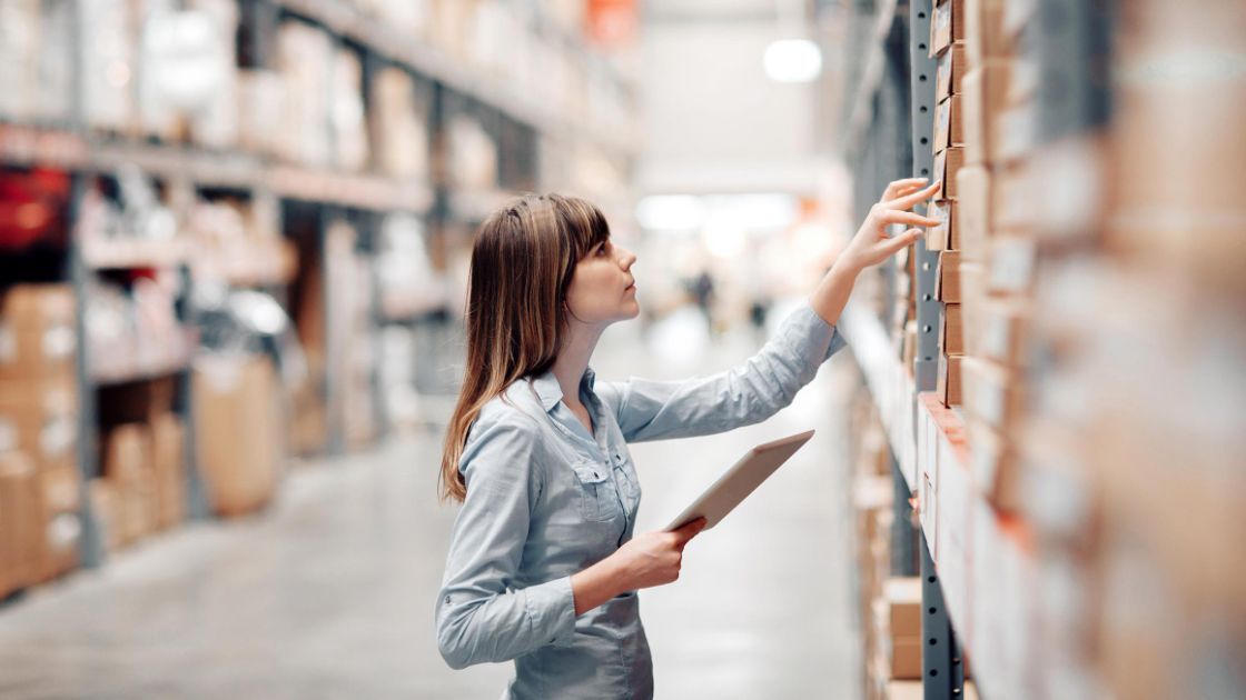 Retail worker checking stock inventory on a tablet in a warehouse aisle
