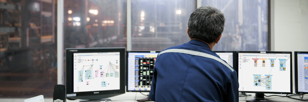 Operator monitoring smart grid control dashboards on multiple screens in an industrial control room