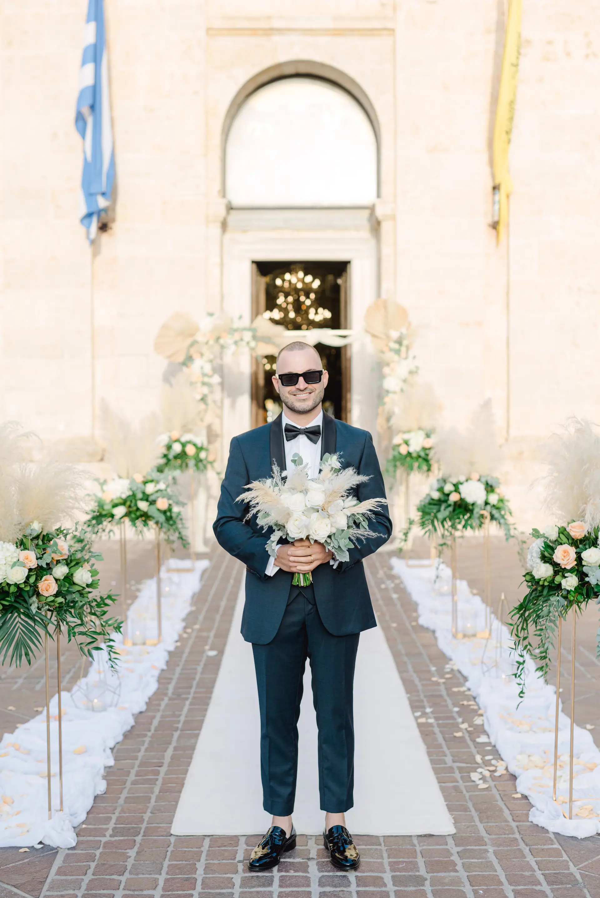 Stylish groom holding the wedding bouquet in front of the church, waiting for the bride.