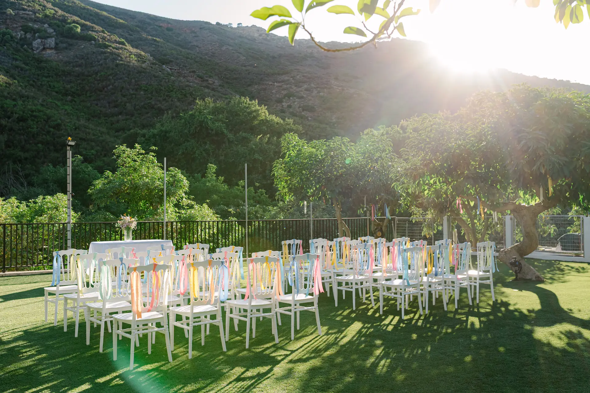 A group of wedding chairs decorated with ribbons in an outdoor yard setup.