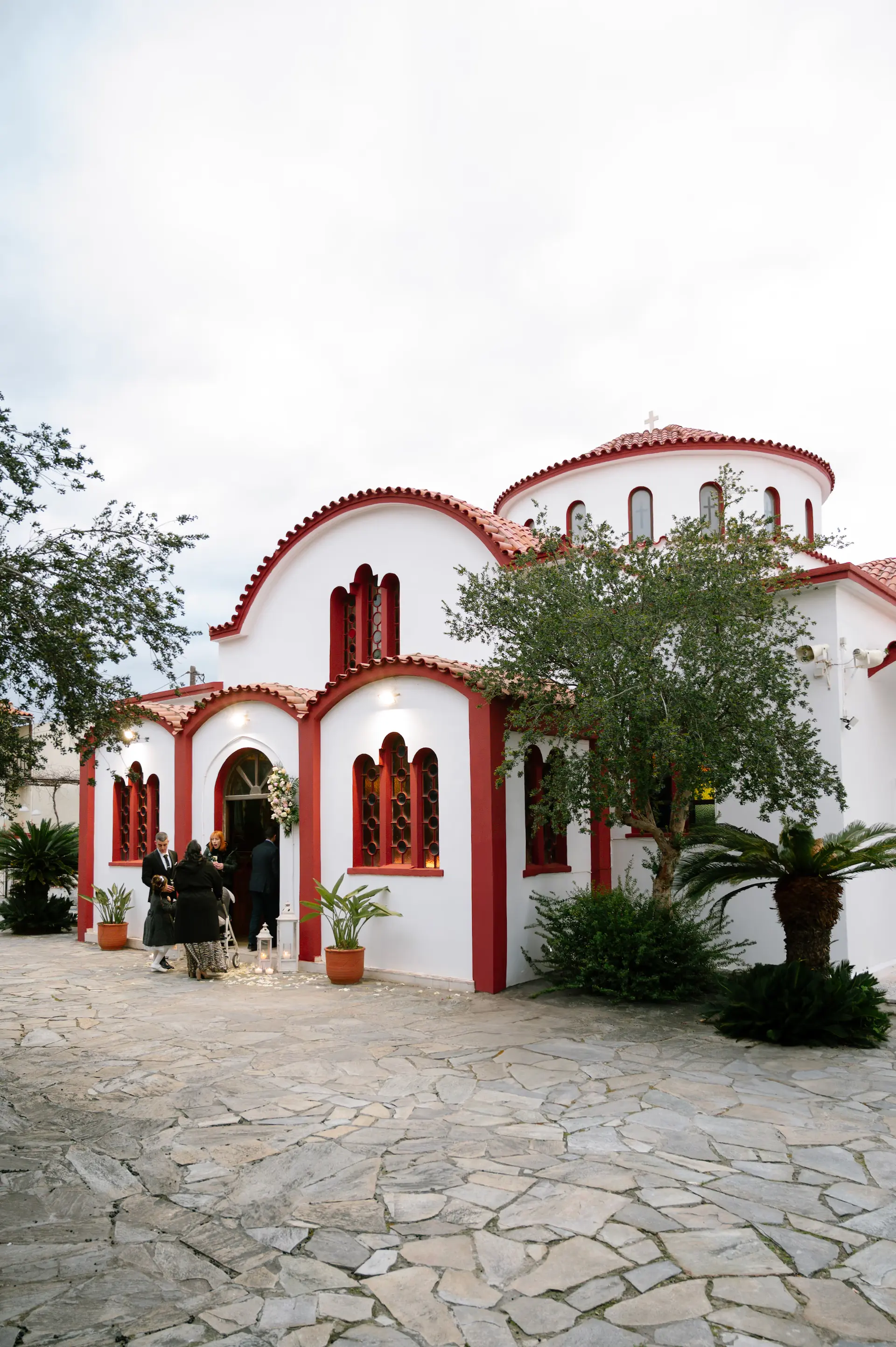 Exterior view of a traditional Greek Orthodox church with stone architecture and a scenic bell tower under a blue sky.