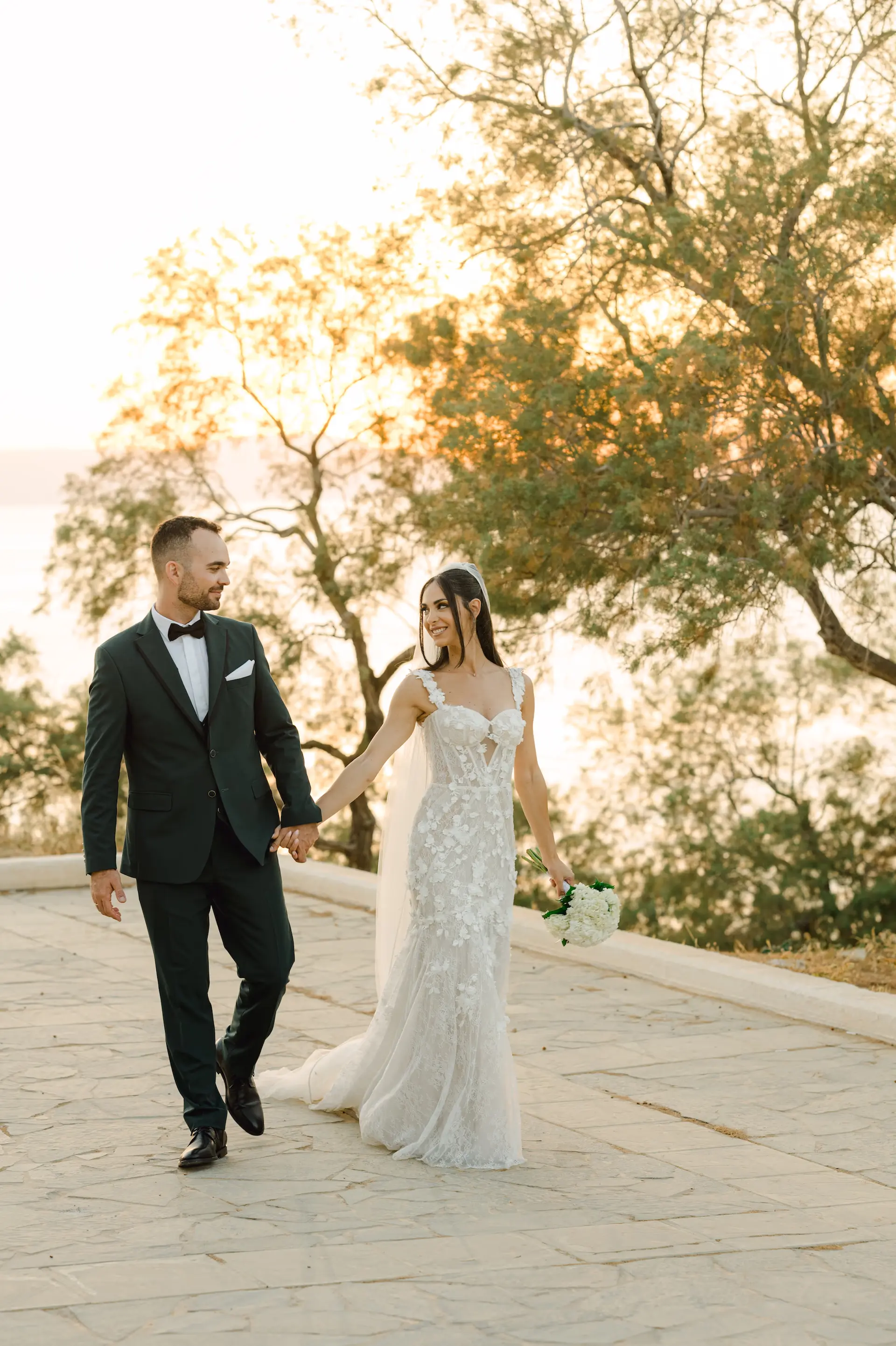 bride and groom holding hands and walking down a path together. φωτογράφος γάμου