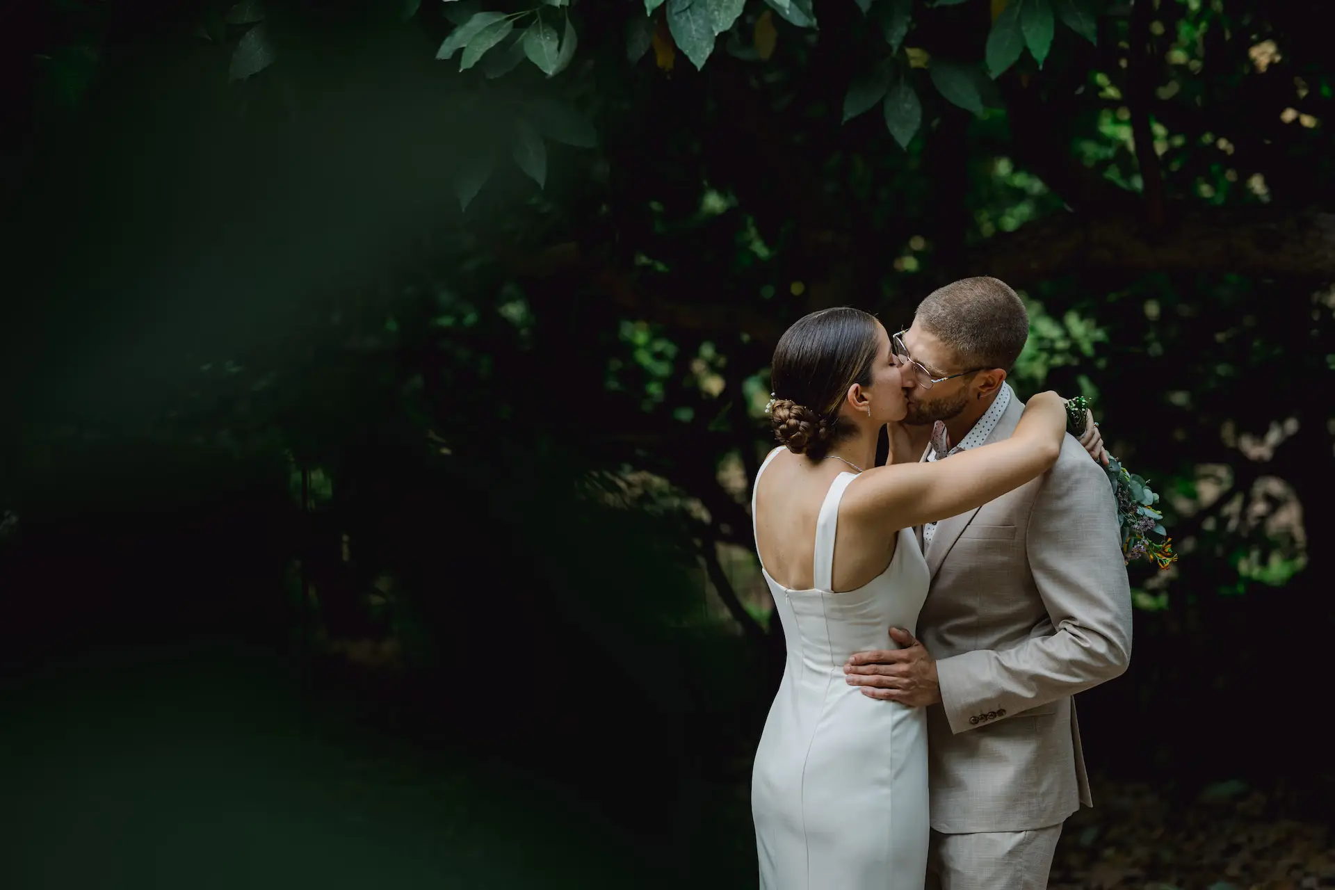 Bride and groom kissing between avocado trees.