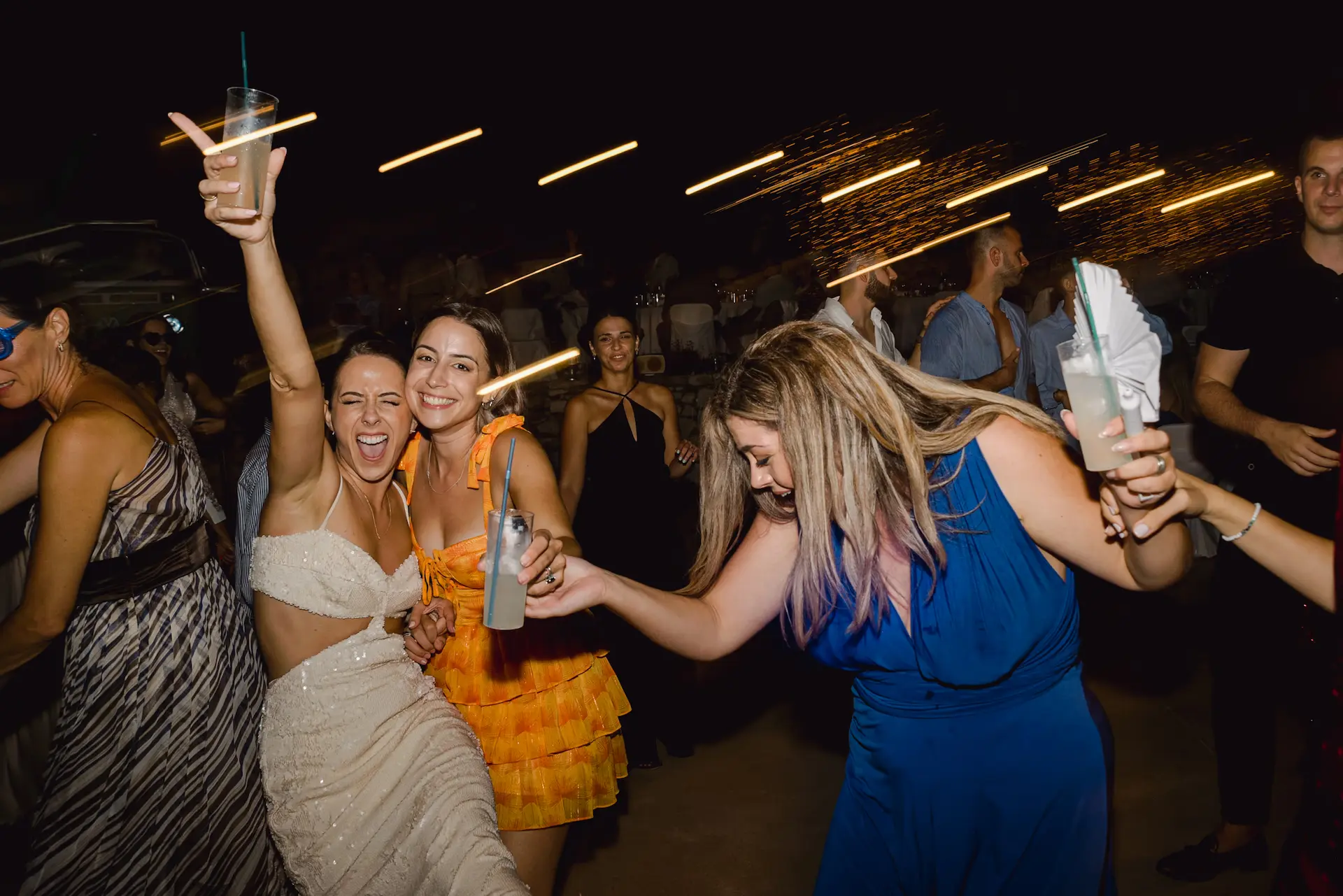a group of women dancing with drinks at the wedding party
