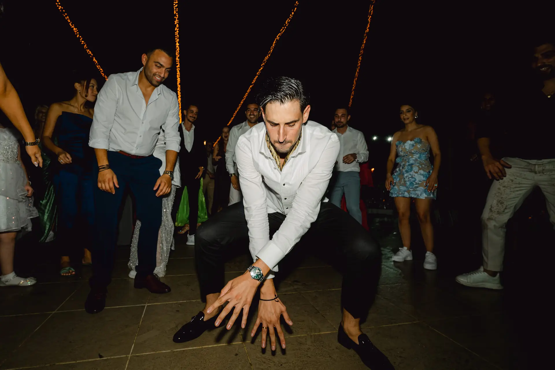 groom squatting on a tile floor with other people in the background