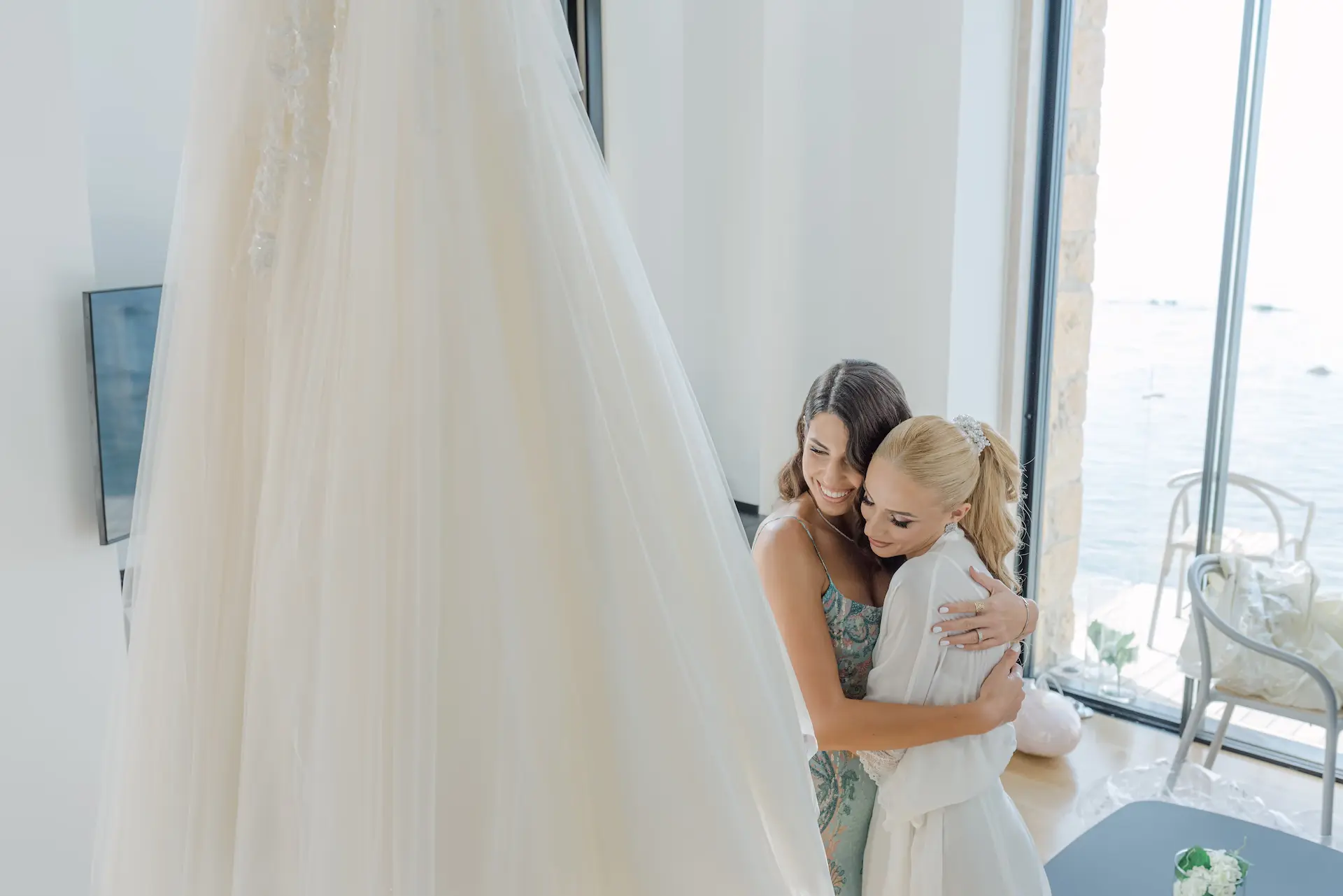bride and her friend hugging in front of a wedding dress