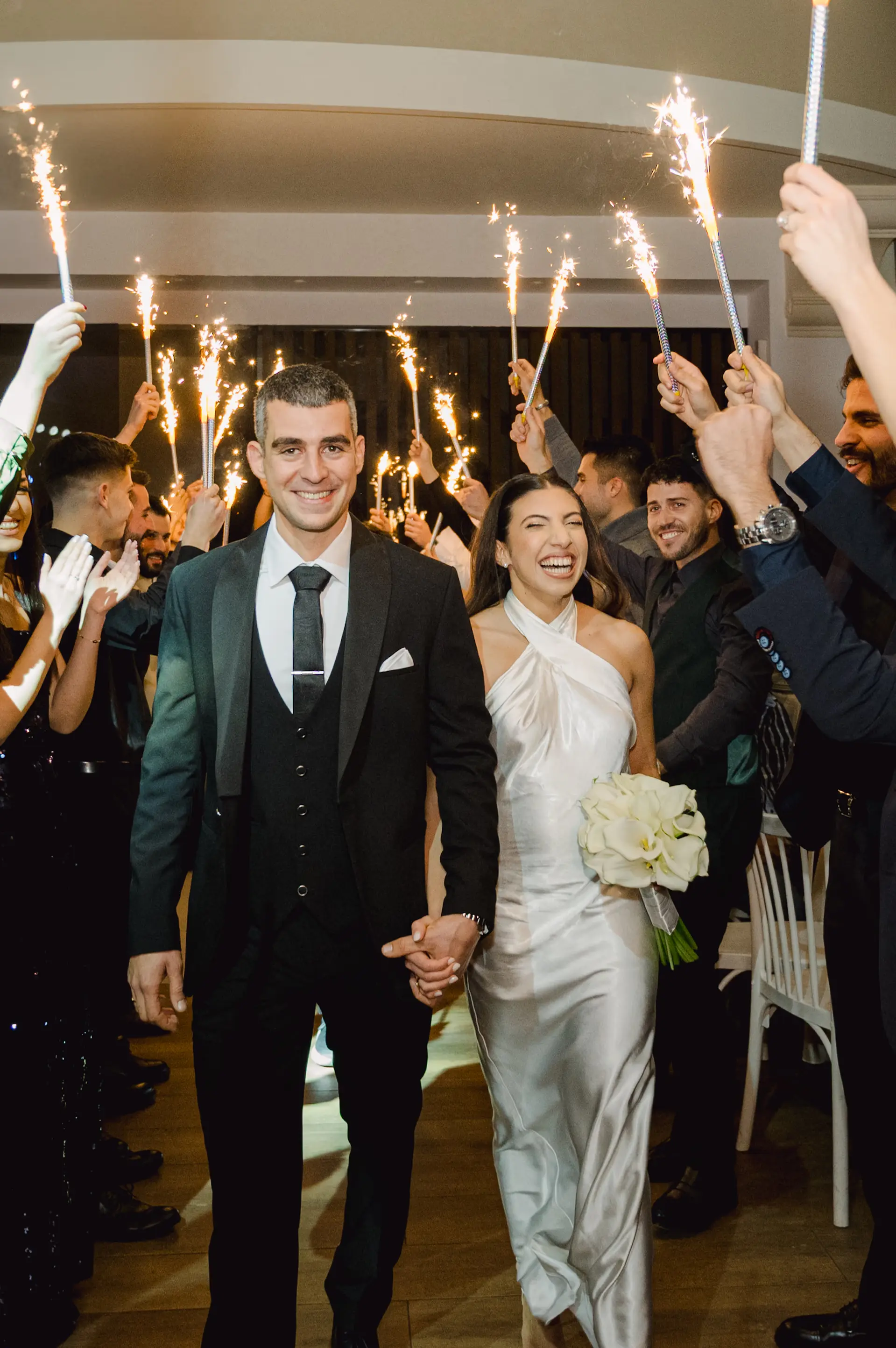 Happy bride and groom walking into their wedding reception under an arch of sparklers held by cheering friends.