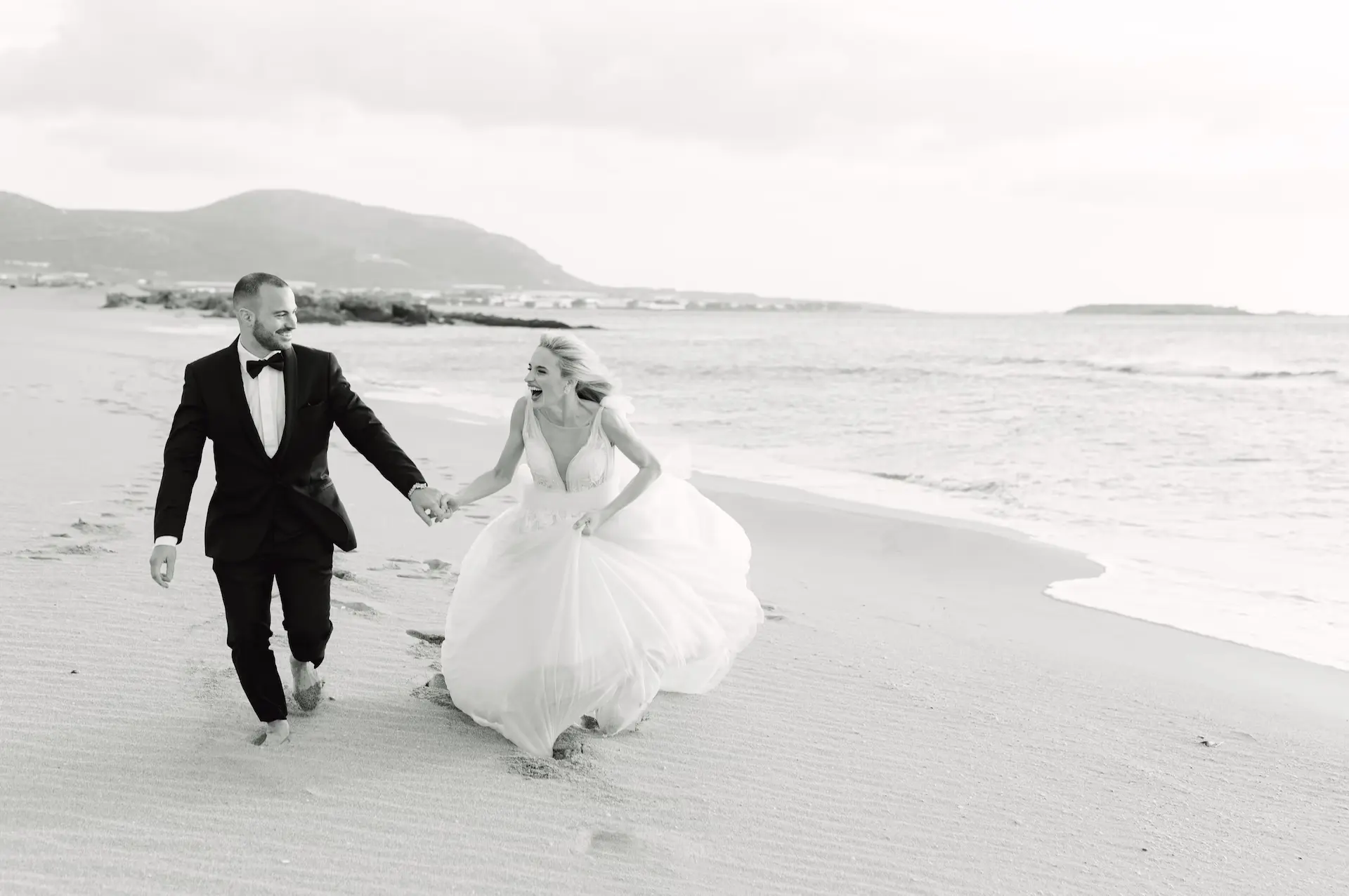 Joyful bride and groom running freely along the shore of Falasarna beach.