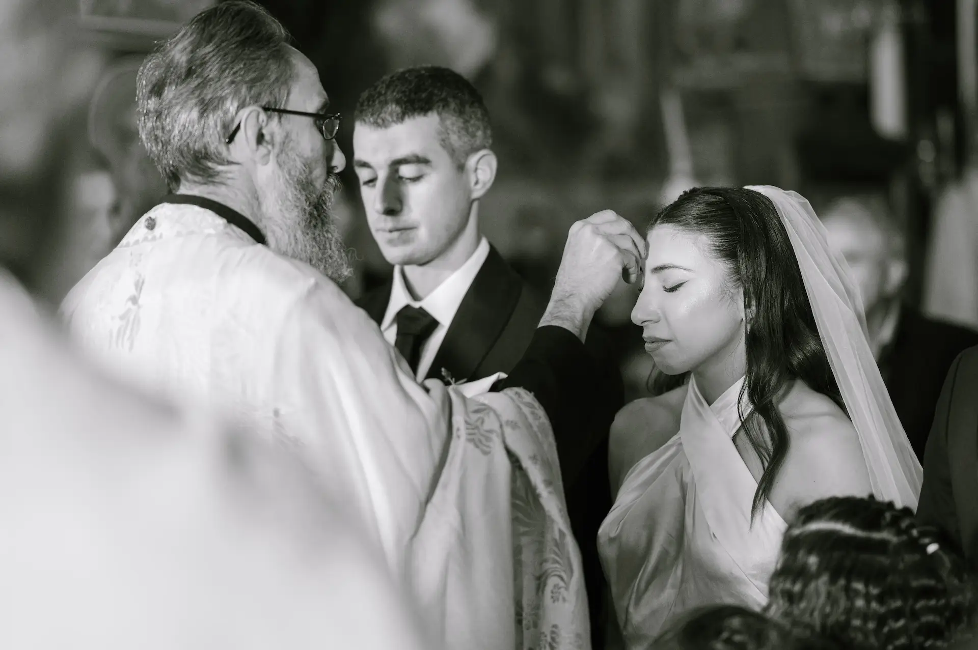 Detailed black and white photography capturing the close-up moment when the priest exchanges the wedding rings on the couple during the ceremony.