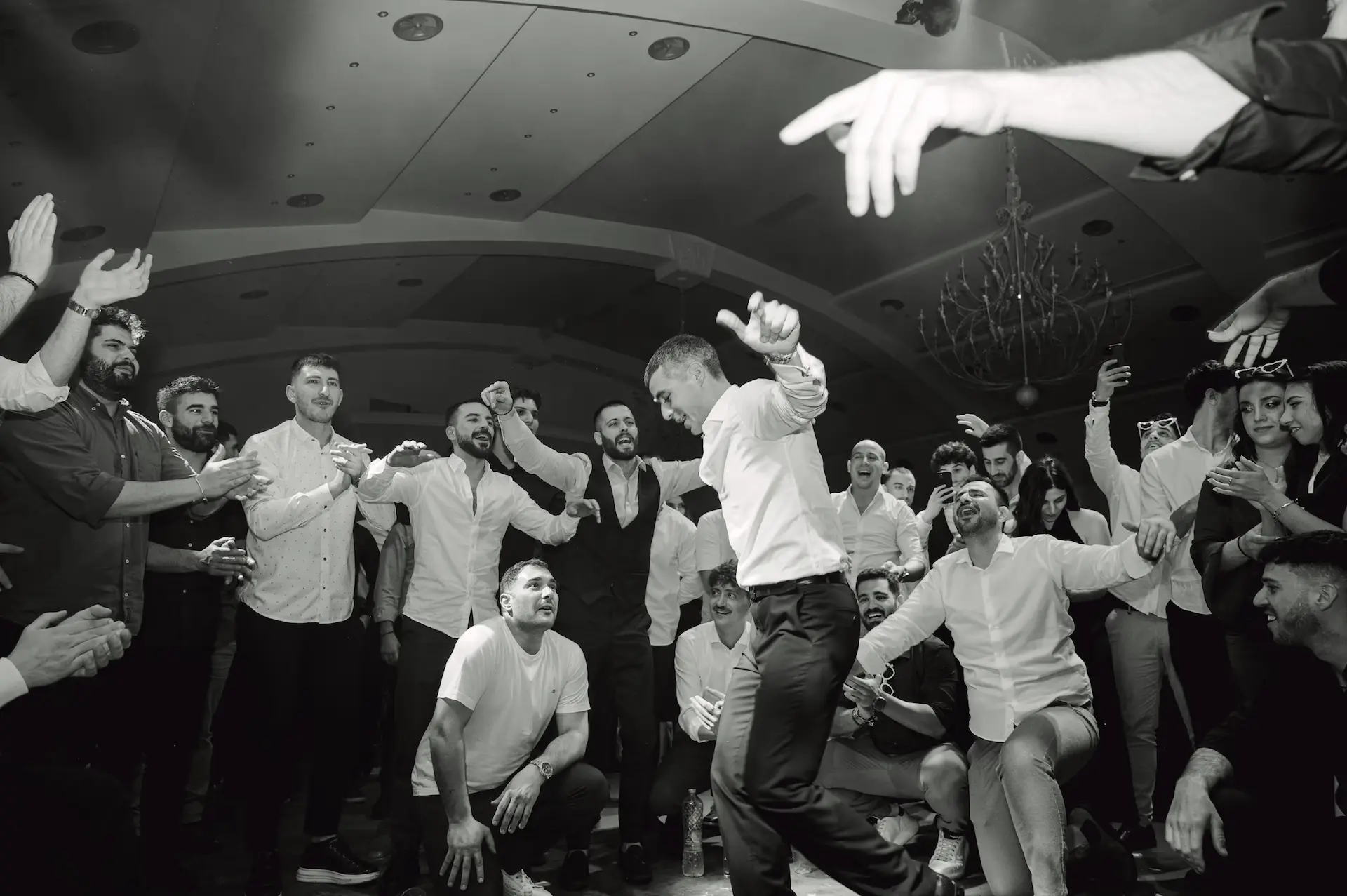 Groom dancing energetically in the middle of the dance floor while guests surround and cheer him on.