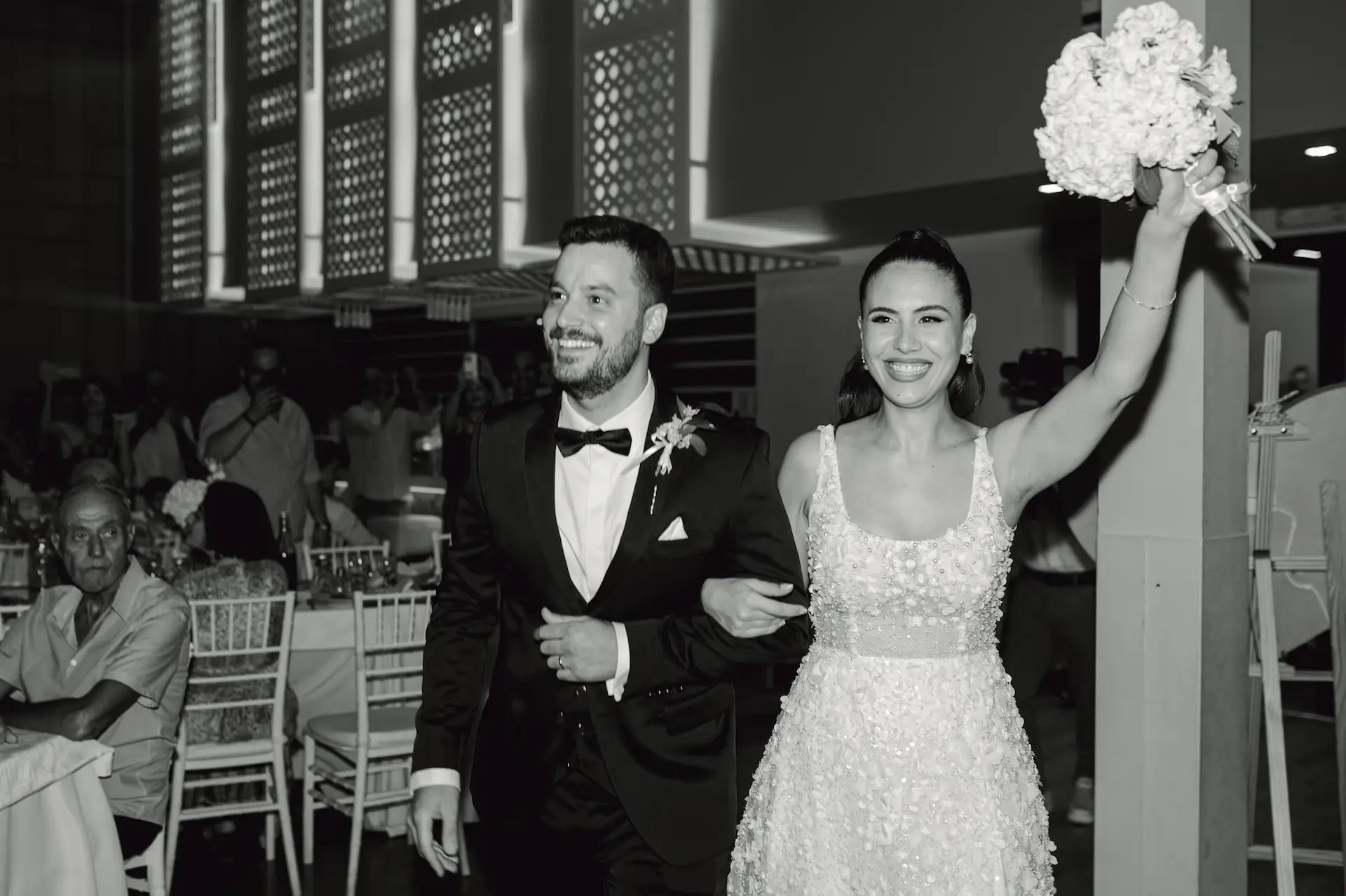 Black and white wedding photography capturing a couple happily entering their venue with smiles and open arms.