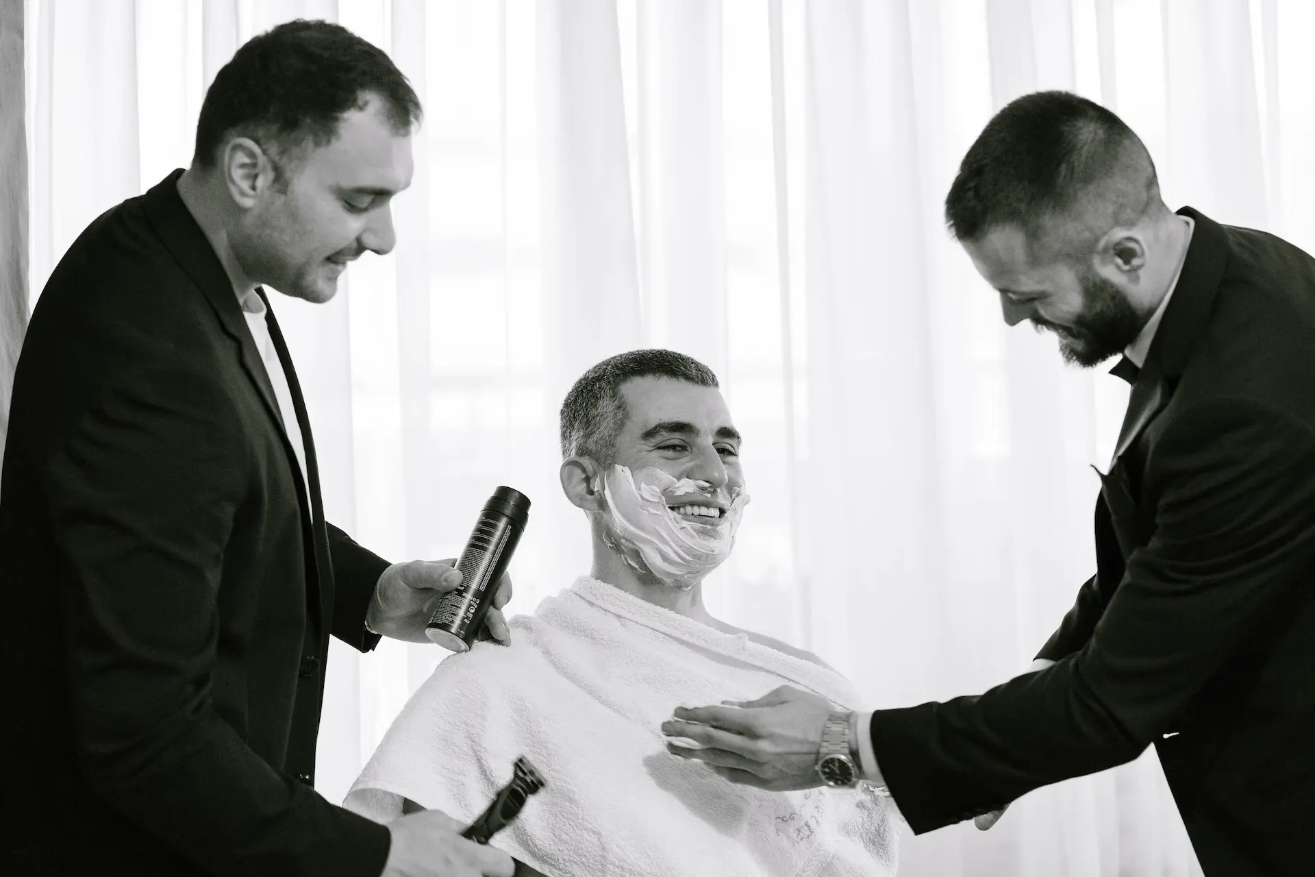 Groom laughing while being traditionally shaved by his friends during his wedding preparation.