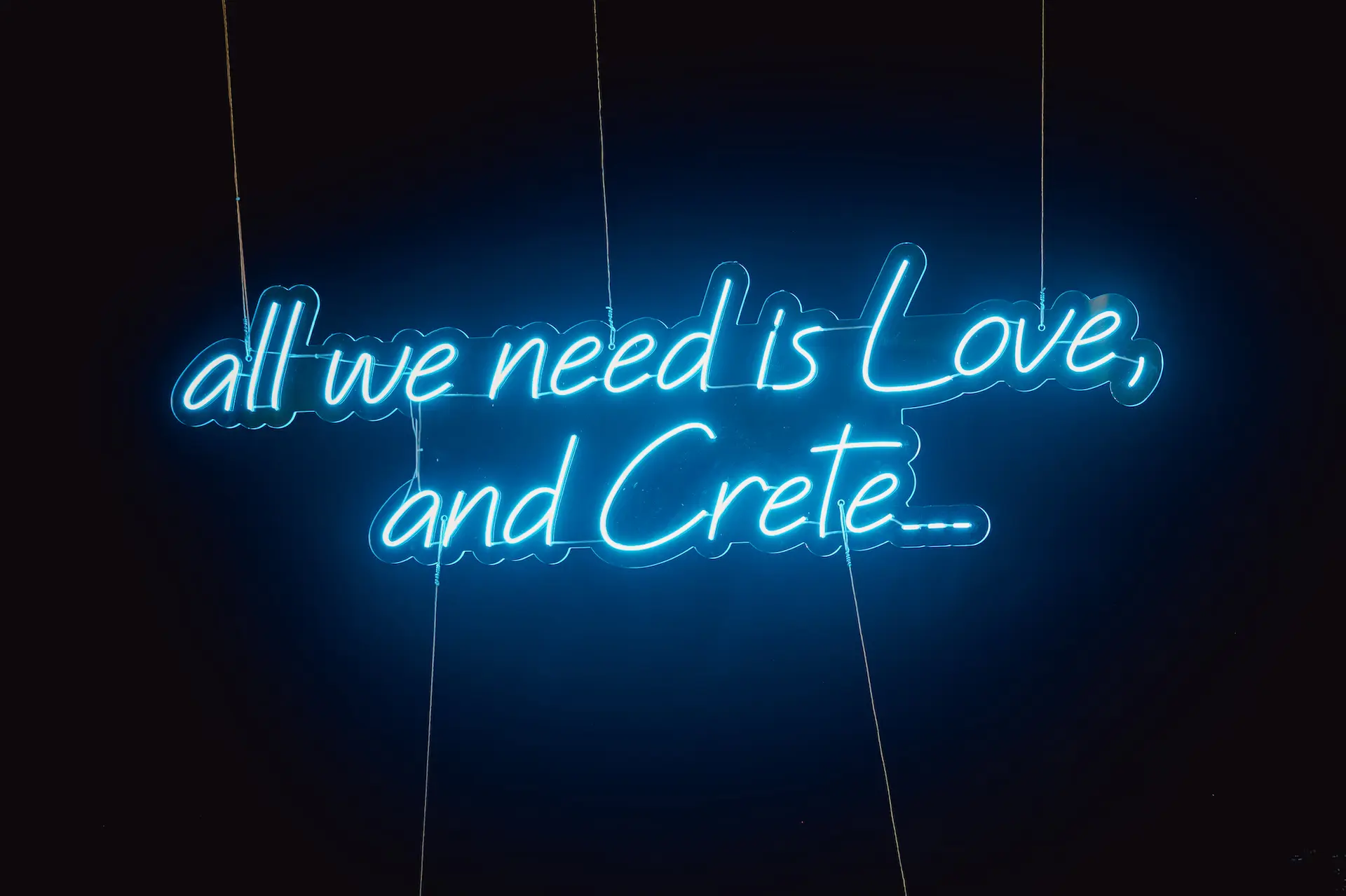a blue neon sign with white text which says "all we need is love, and Crete"