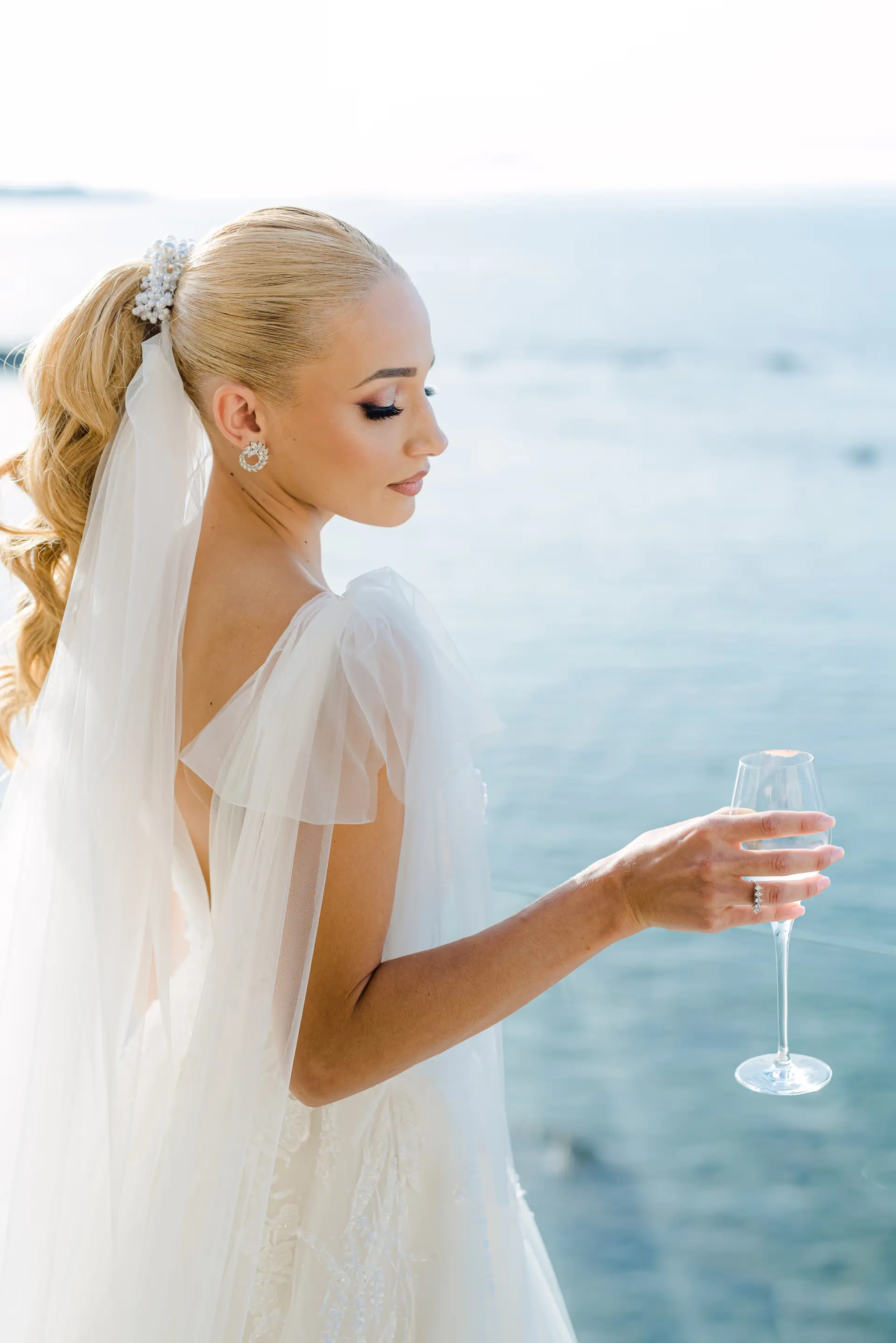 bride holding a glass of wine with the blue sea as a scenic background.